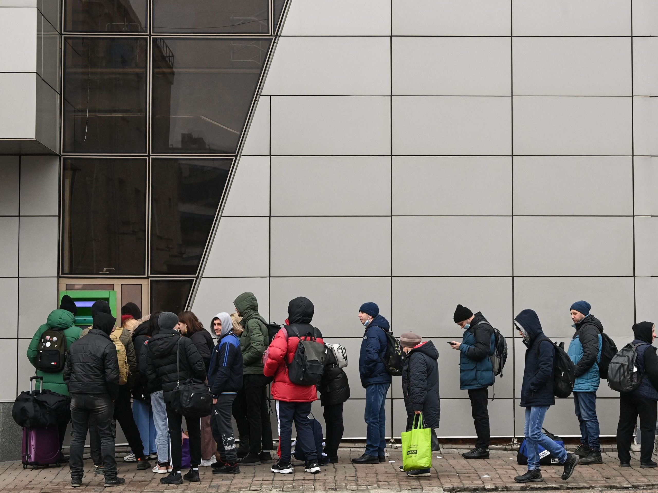 People wait in line to access an ATM.