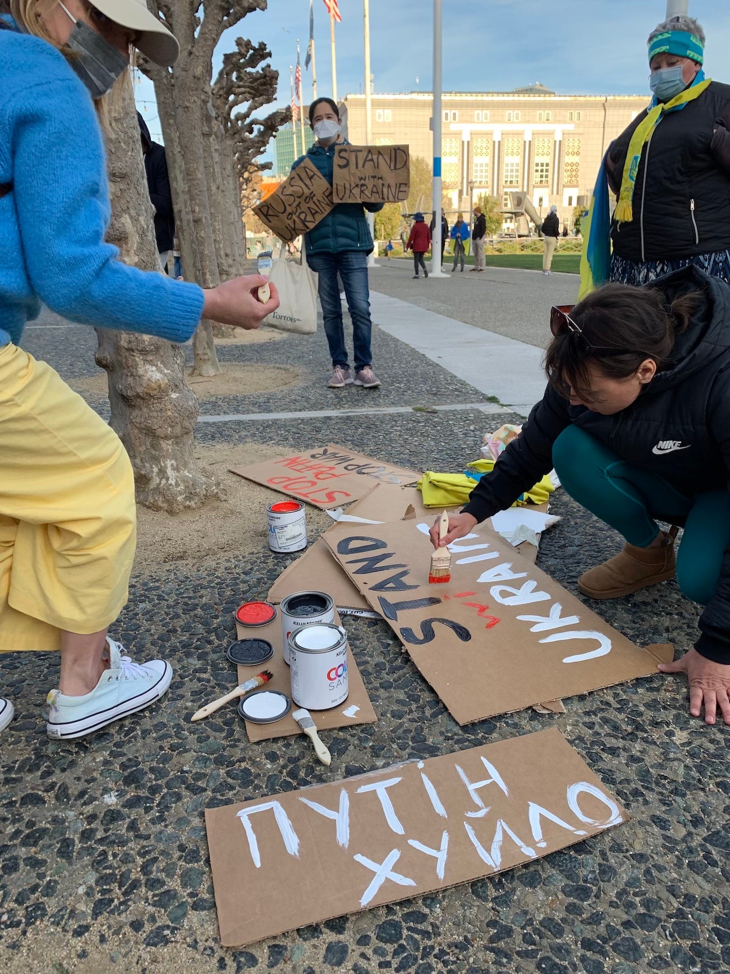 young woman paints "stand with ukraine" sign on cardboard on the ground