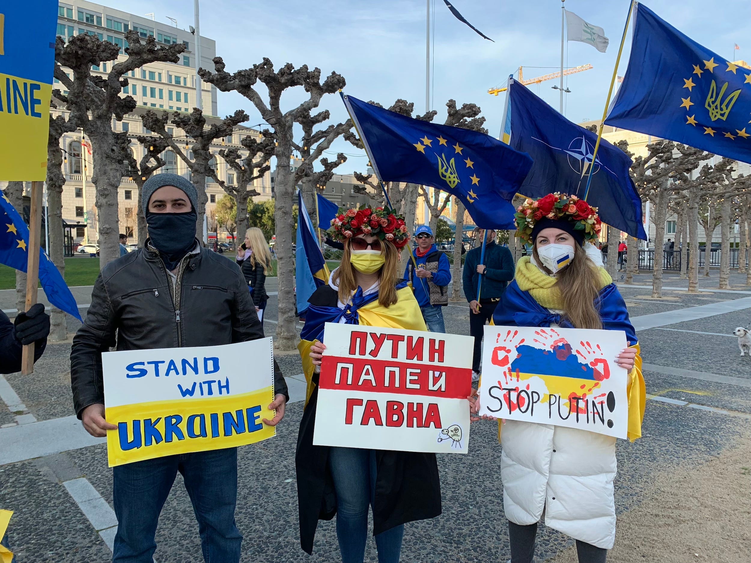 three masked protestors pose with pro-ukraine and anti-putin signs