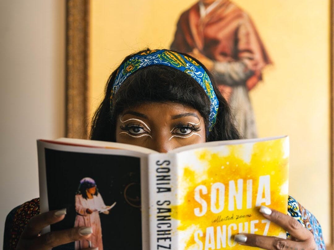 A person in a blue headband smiles with a book in front of her mouth