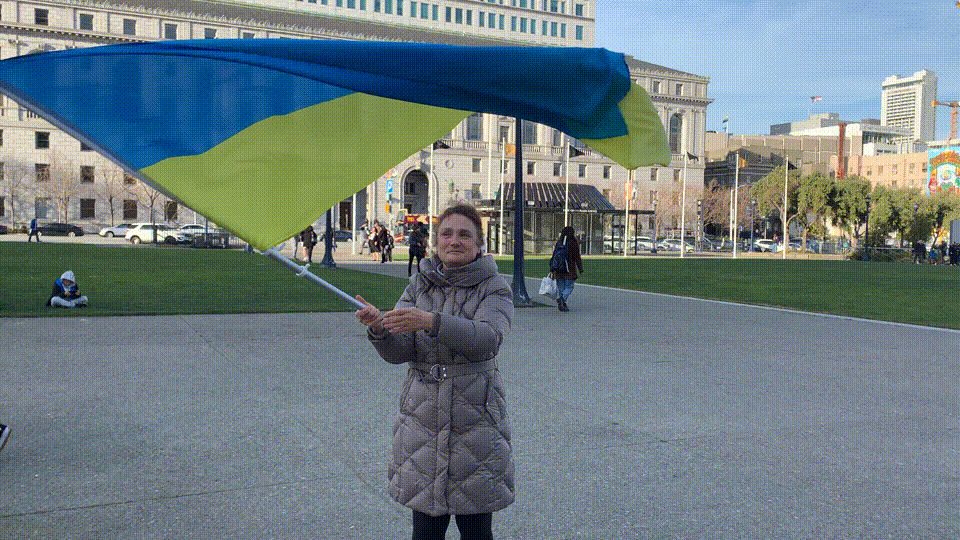 woman in grey coat waves ukrainian flag blue and yellow in a city square