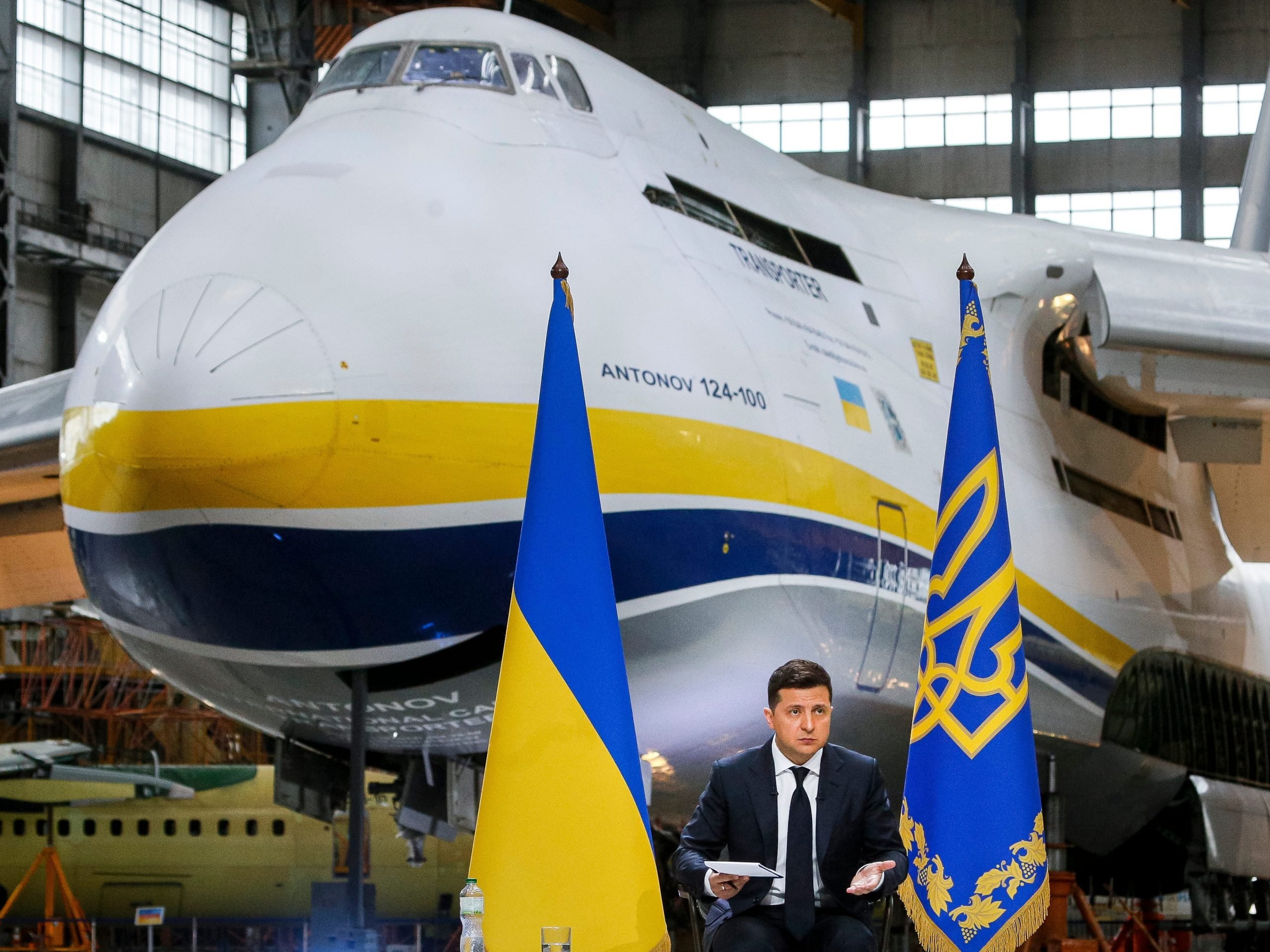 Ukrainian President Volodymyr Zelenskyy standing in front of the world's largest airplane, the Antonov An-225 Mriya.