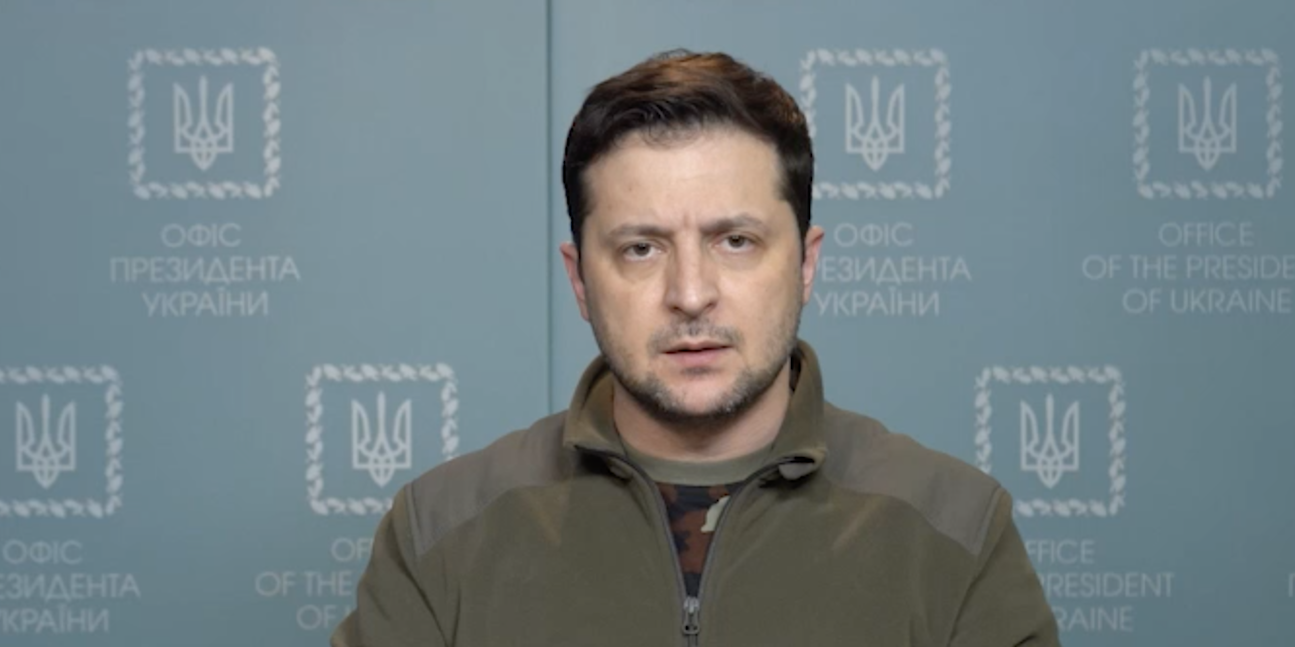 President Volodymyr Zelensky in a video address released February 28, 2022. He is at a podium with a Ukrainian flag nearby.