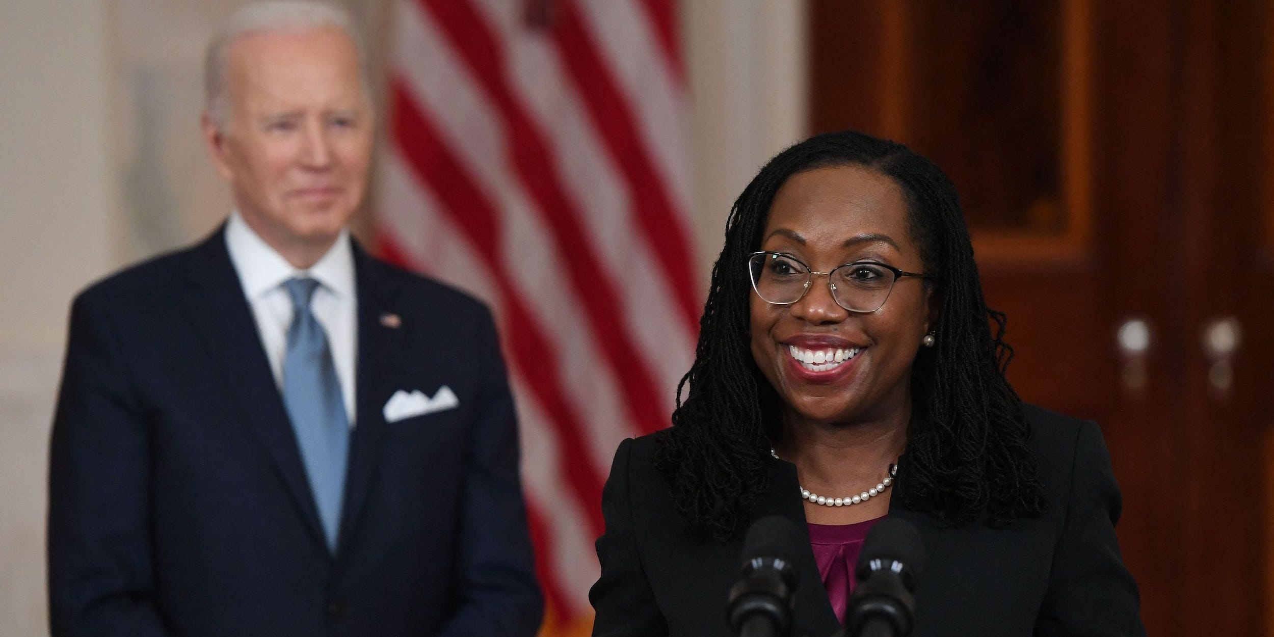 Judge Ketanji Brown Jackson stands in front of President Joe Biden and speaks from a podium after being nominated for Associate Justice of the US Supreme Court, in the Cross Hall of the White House.