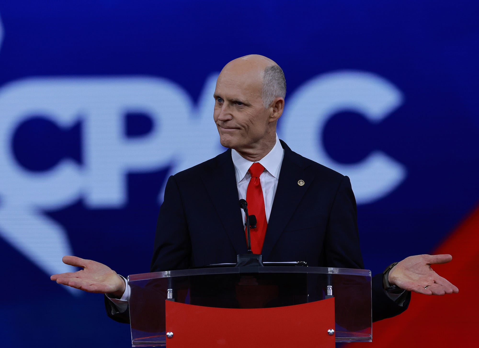 Republican Sen. Rick Scott of Florida, sporting a dark suit, white shirt, and bright red tie, stands with his hands open wide during a speech before the Conservative Political Action Conference in Orlando, Florida.
