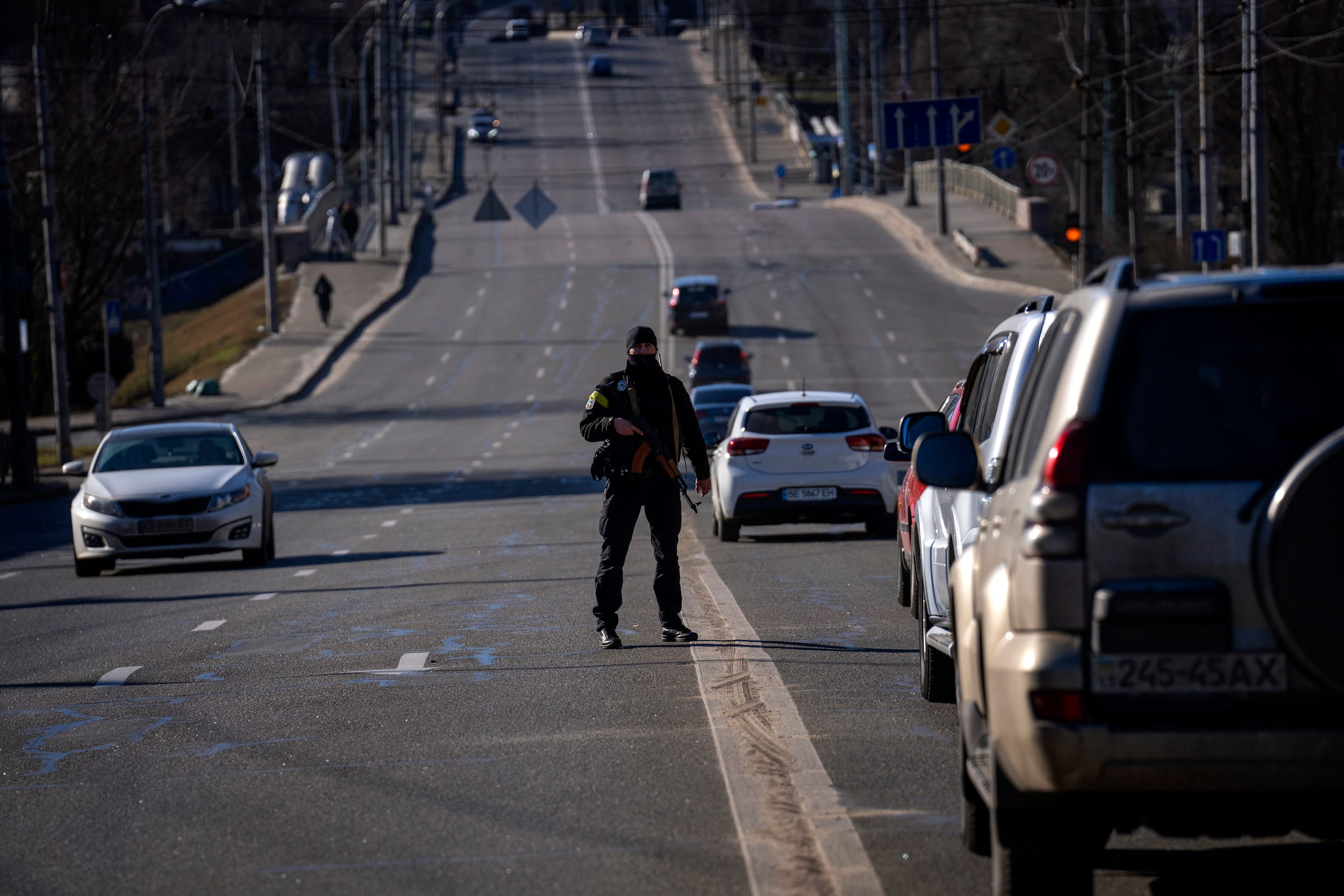 armed police officer stands on a street outside Kyiv with cars going by