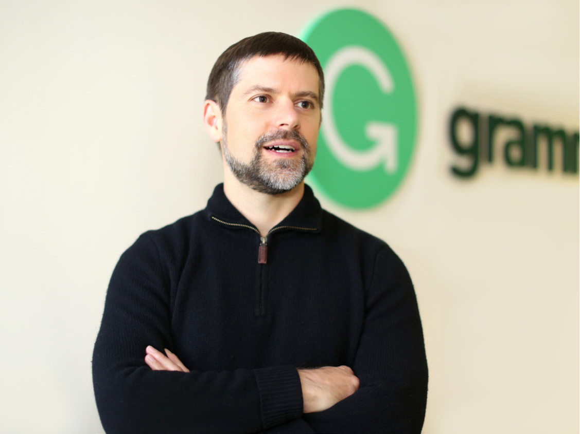 Brad Hoover with his arms crossed standing in front of the Grammarly logo on the wall behind him.