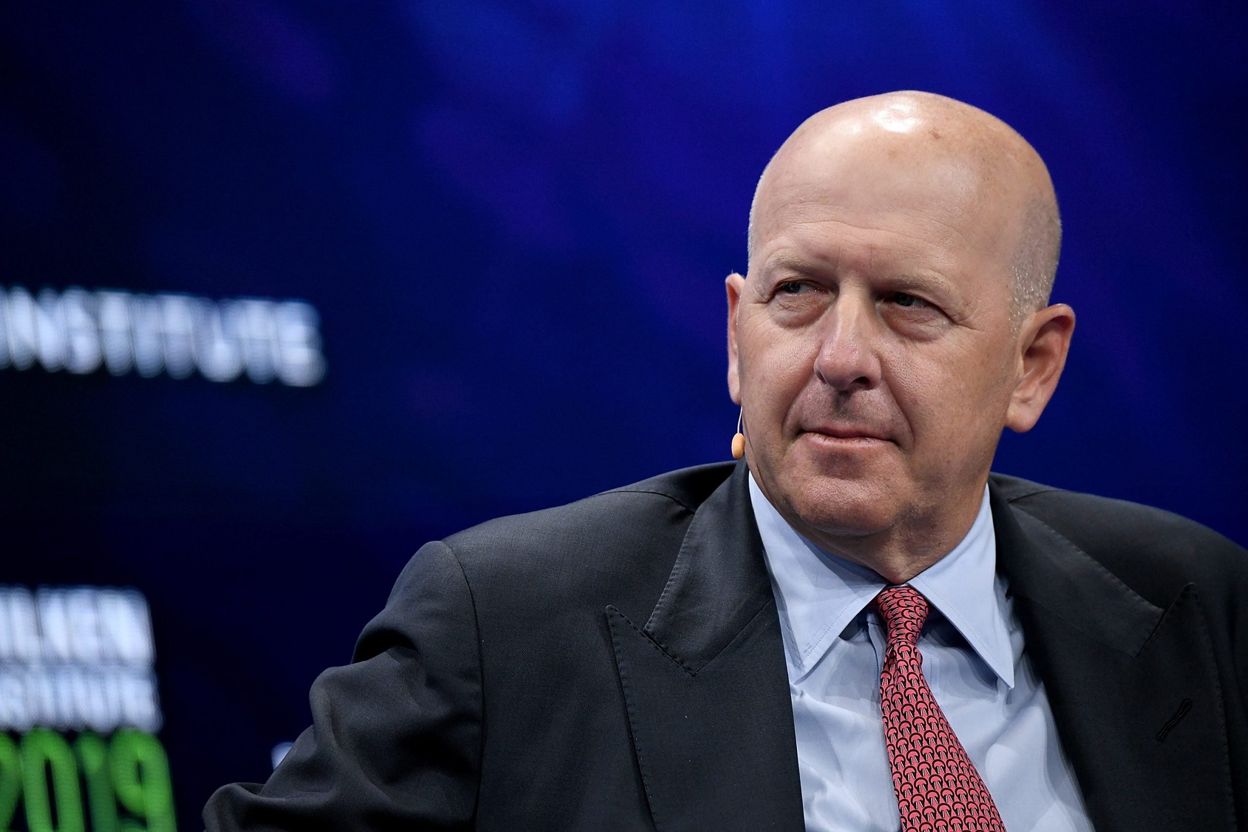 Goldman Sachs CEO David Solomon wears a pale blue shirt and red tie while speaking on stage.