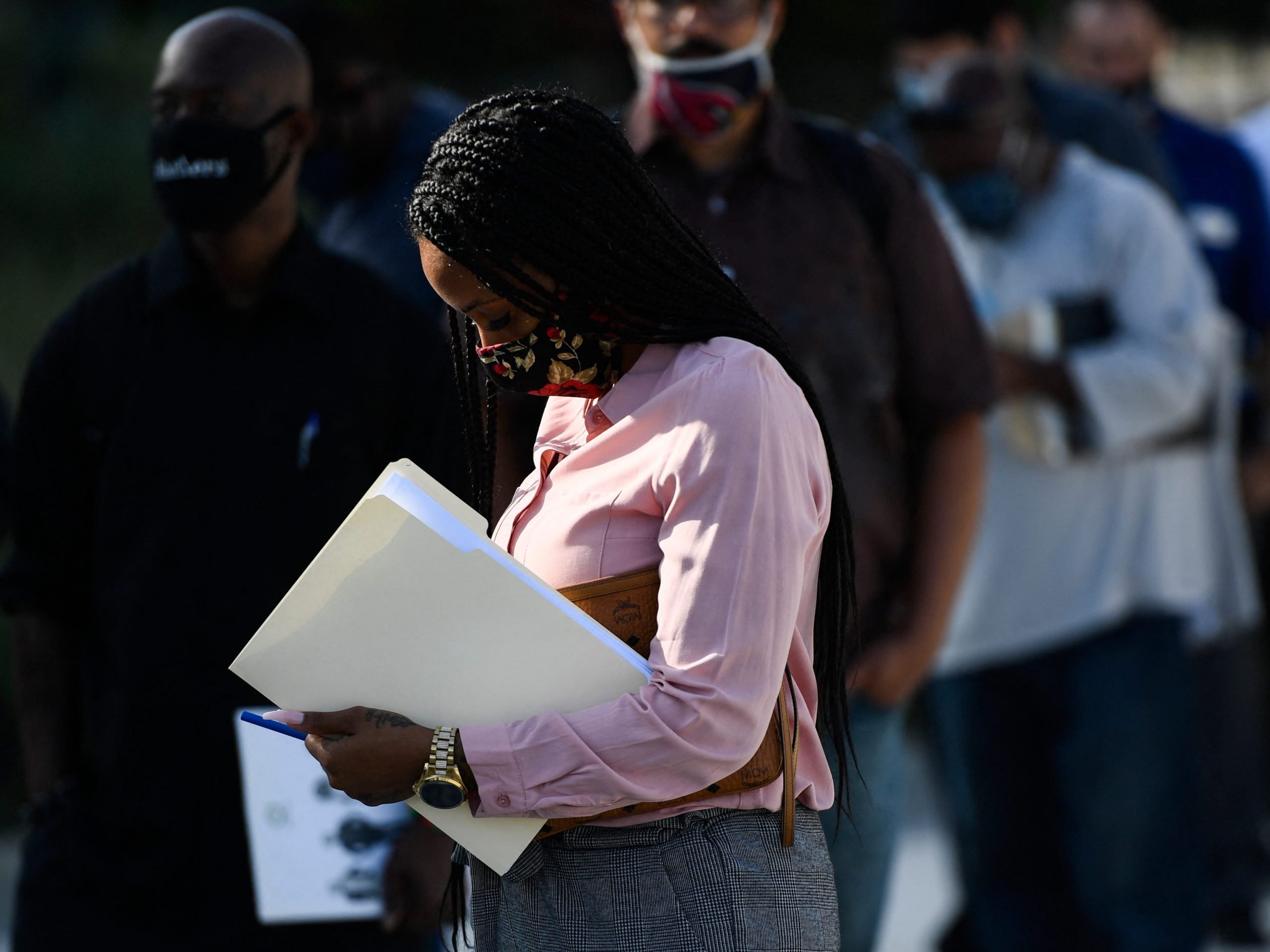 A woman in a pink shirt holds a folder in a line at a job fair in Los Angeles