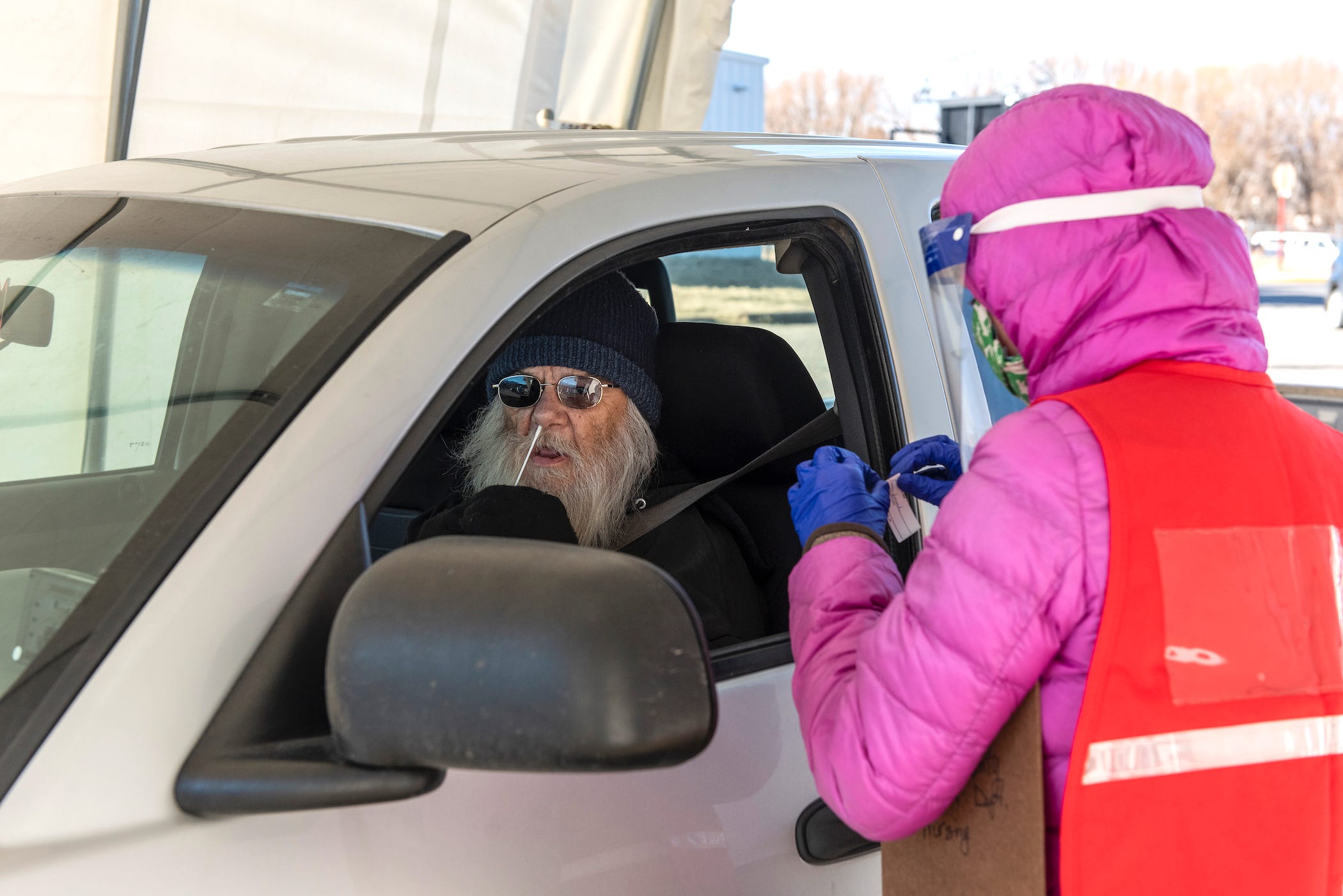 man at drive-thru testing site performs binaxnow rapid test on himself, as attendant waits at his window