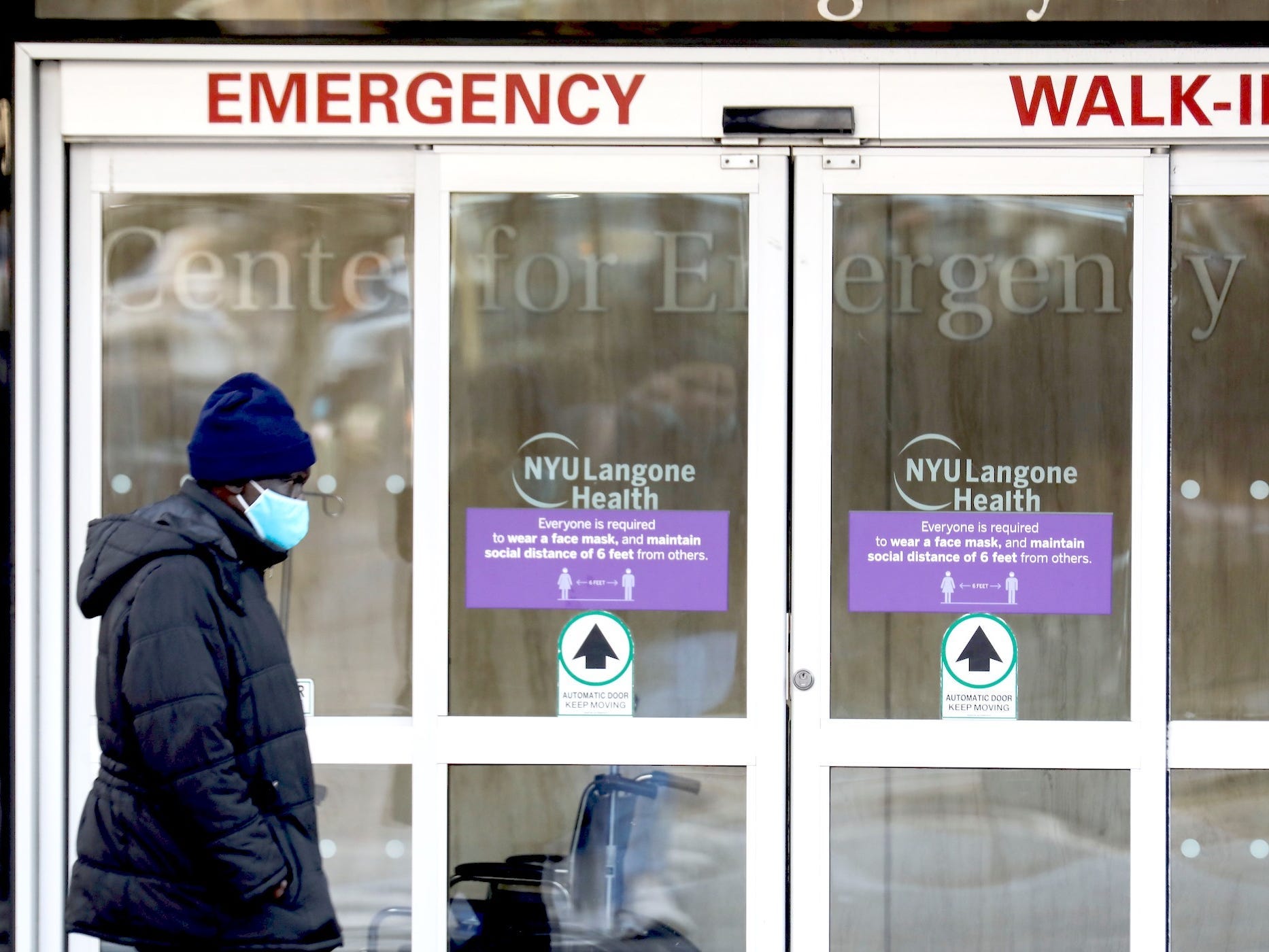 A person wearing a mask walks by the doors for the emergency department ot NYU Langhorne health hospital.