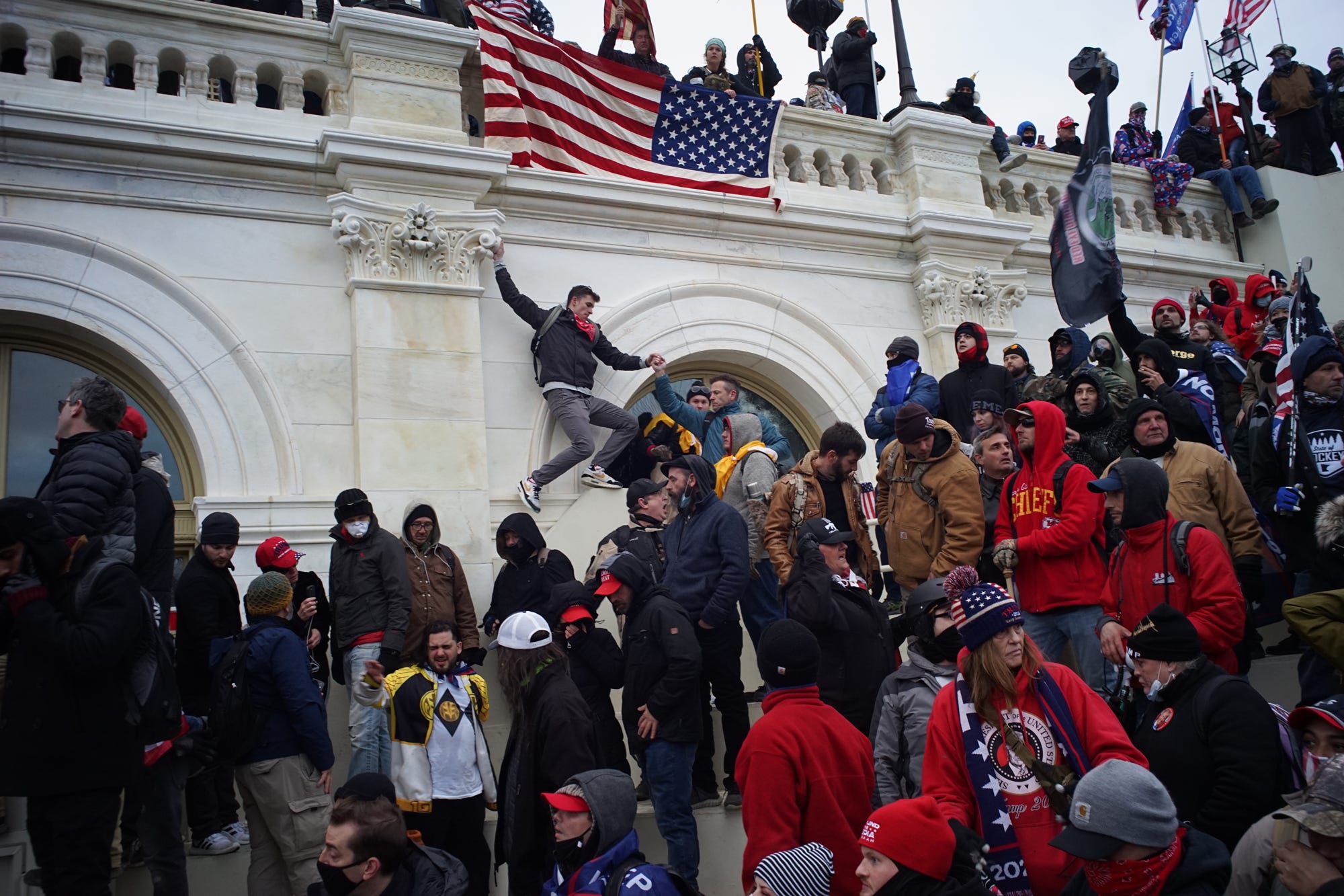 Someone is seen hanging from the Capitol facade beneath an American flag.