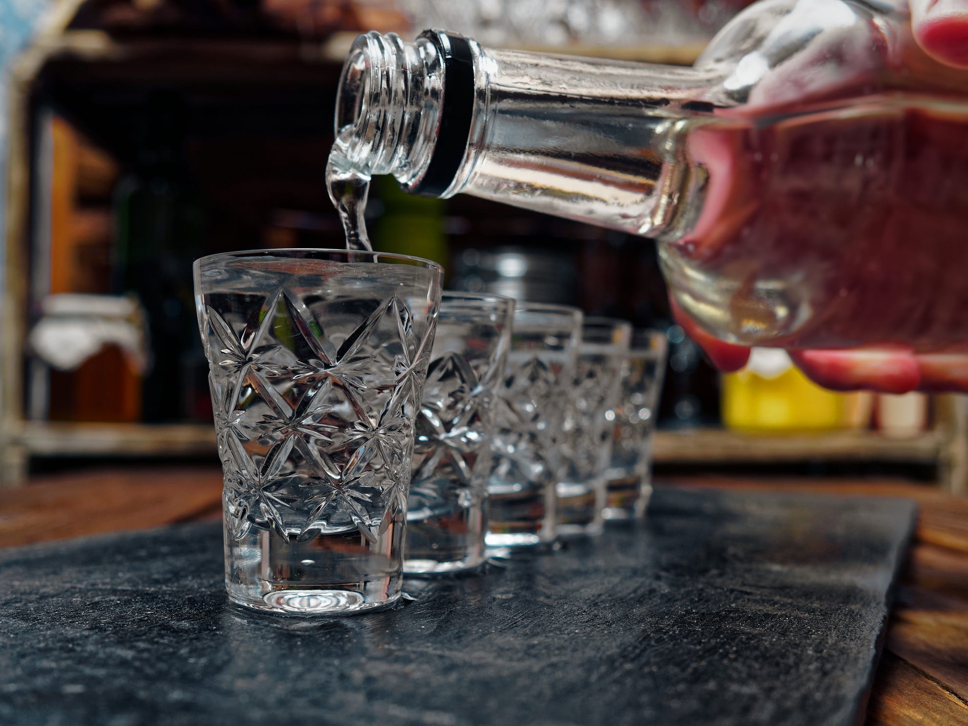 A bottle of vodka being poured into a line of shot glasses