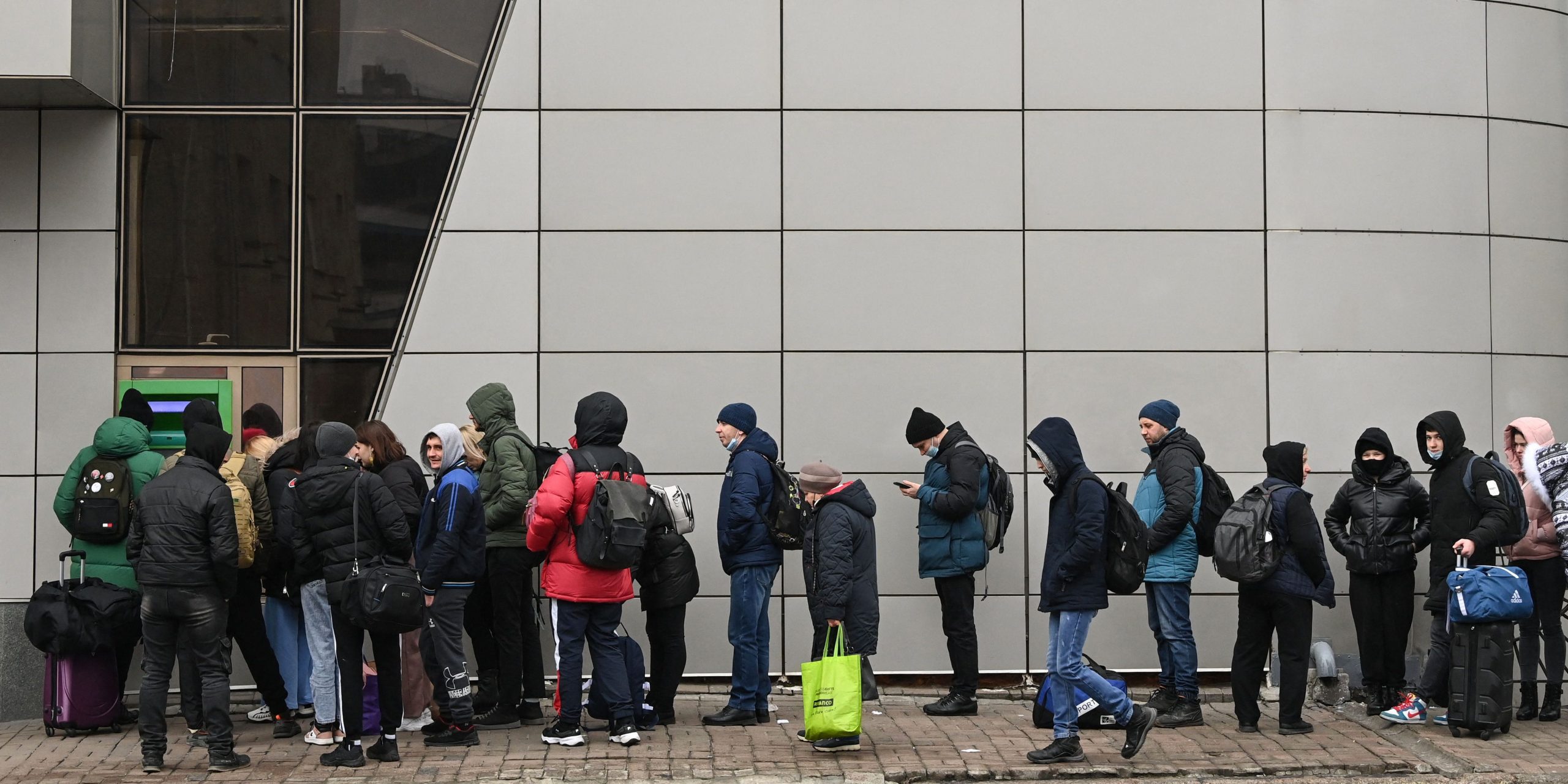 People wait in line to access an ATM.