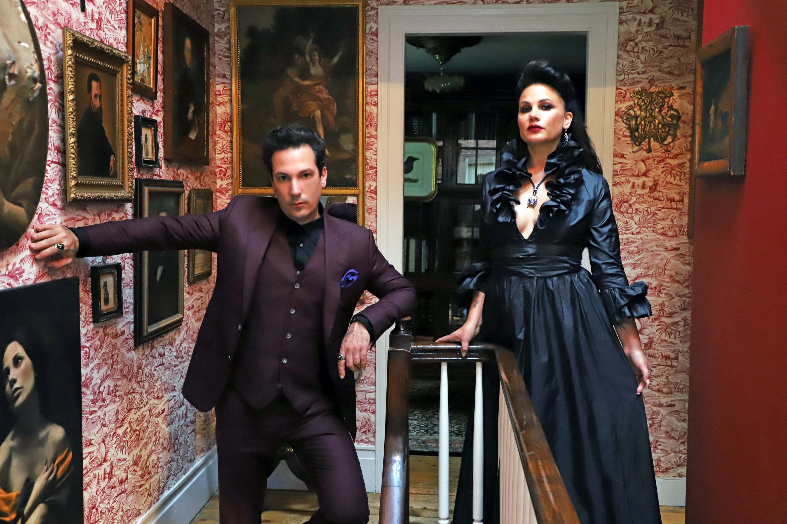 Ryan Matthew Cohn and Regina Cohn posing in front of antique wall art.