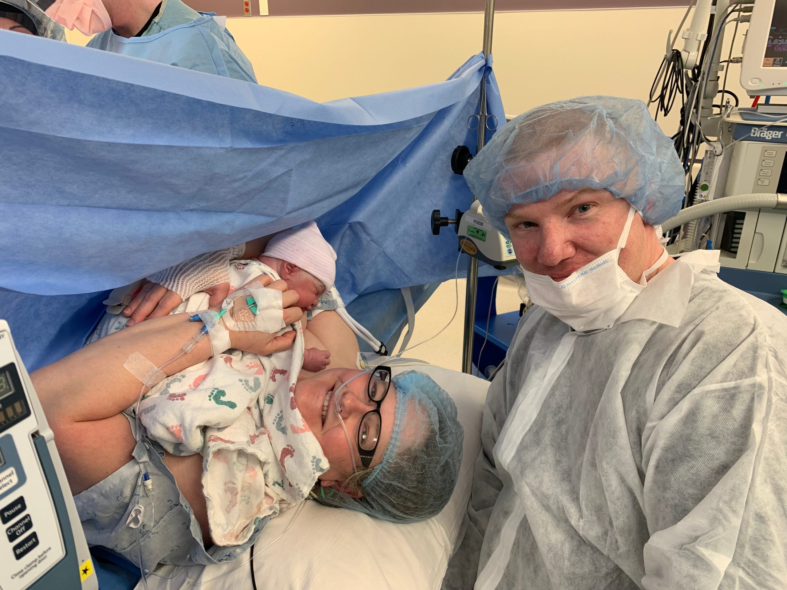 lisa in a hospital bed with her newborn son and her husband after her C-section