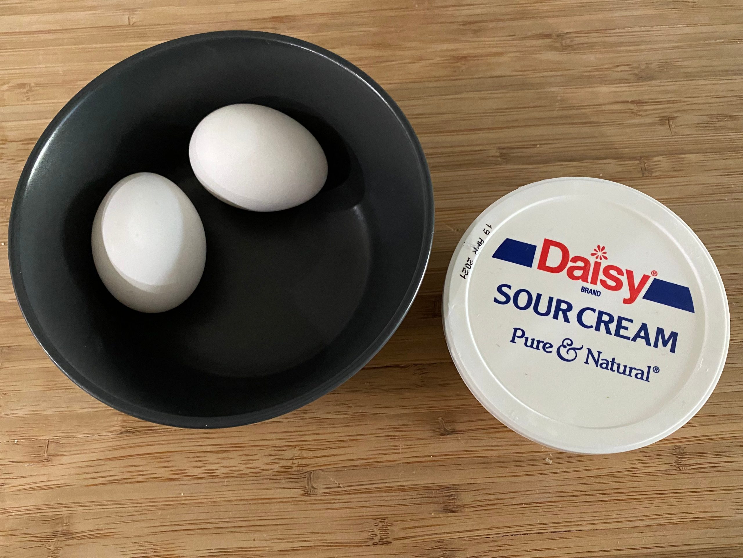 Daisy sour cream and two eggs in a black bowl on a wooden cutting board