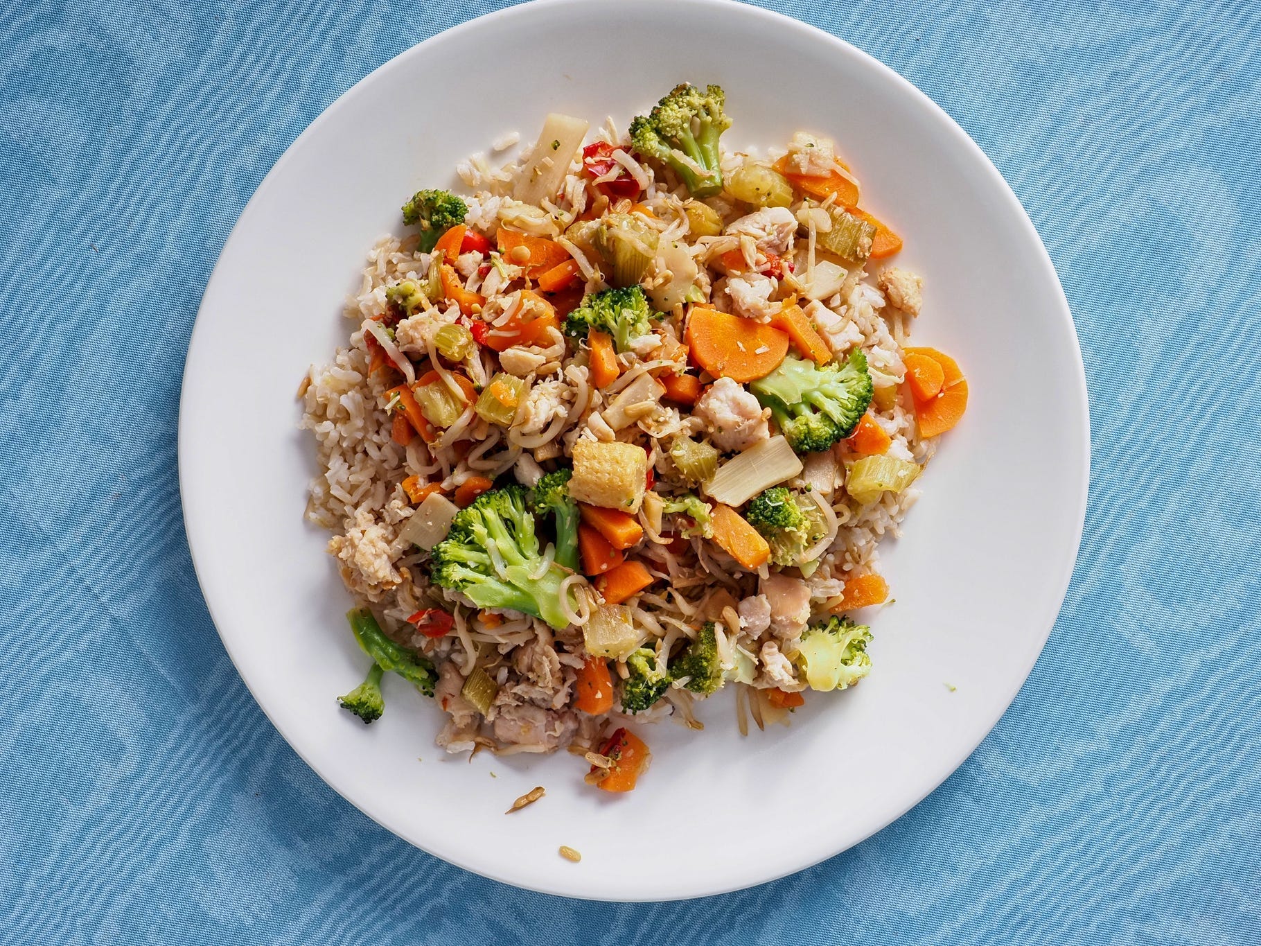 A plate of brown rice with stir fried veggies on a blue tabletop