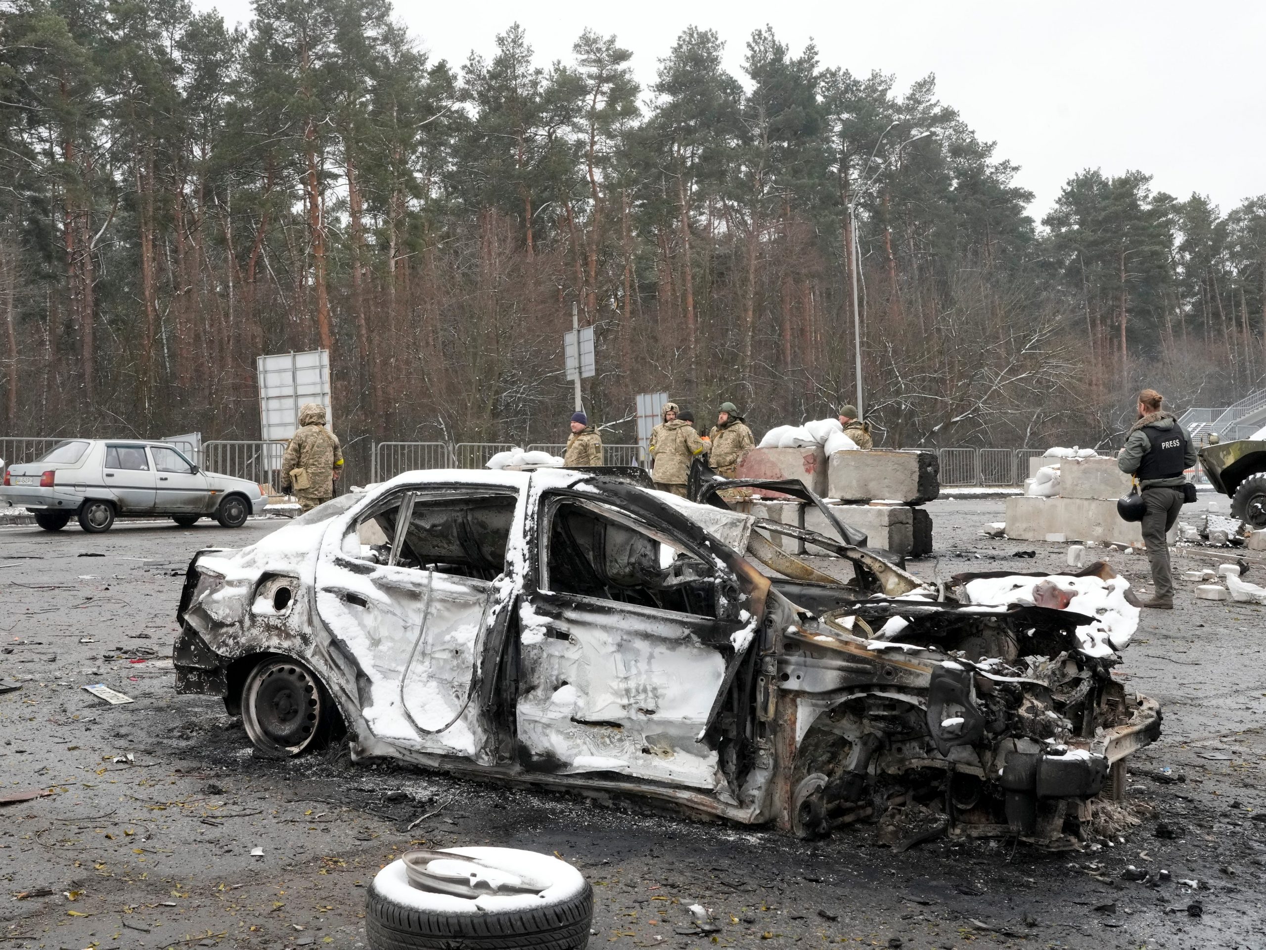 Ukrainian servicemen and volunteers of Ukraine's Territorial Defense Forces stand behind a damaged car at a checkpoint in Brovary, outside Kyiv, Ukraine, Tuesday, March 1, 2022.