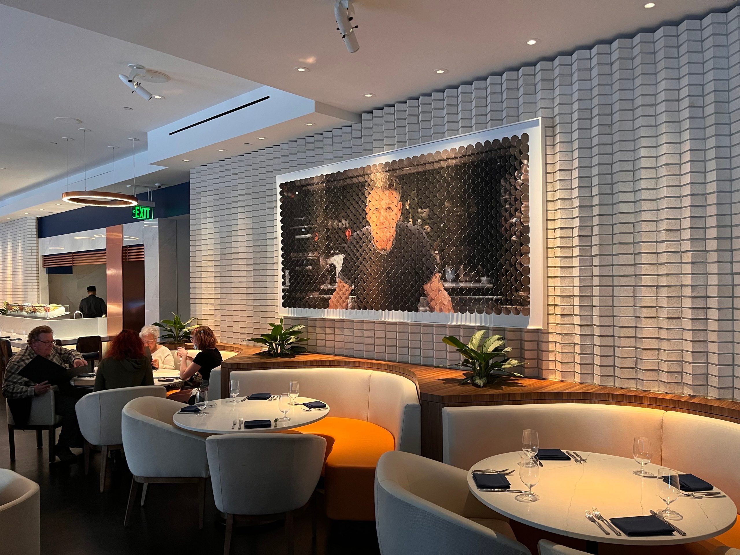 White tables and chairs in restaurant with portrait of Gordon Ramsay on wall