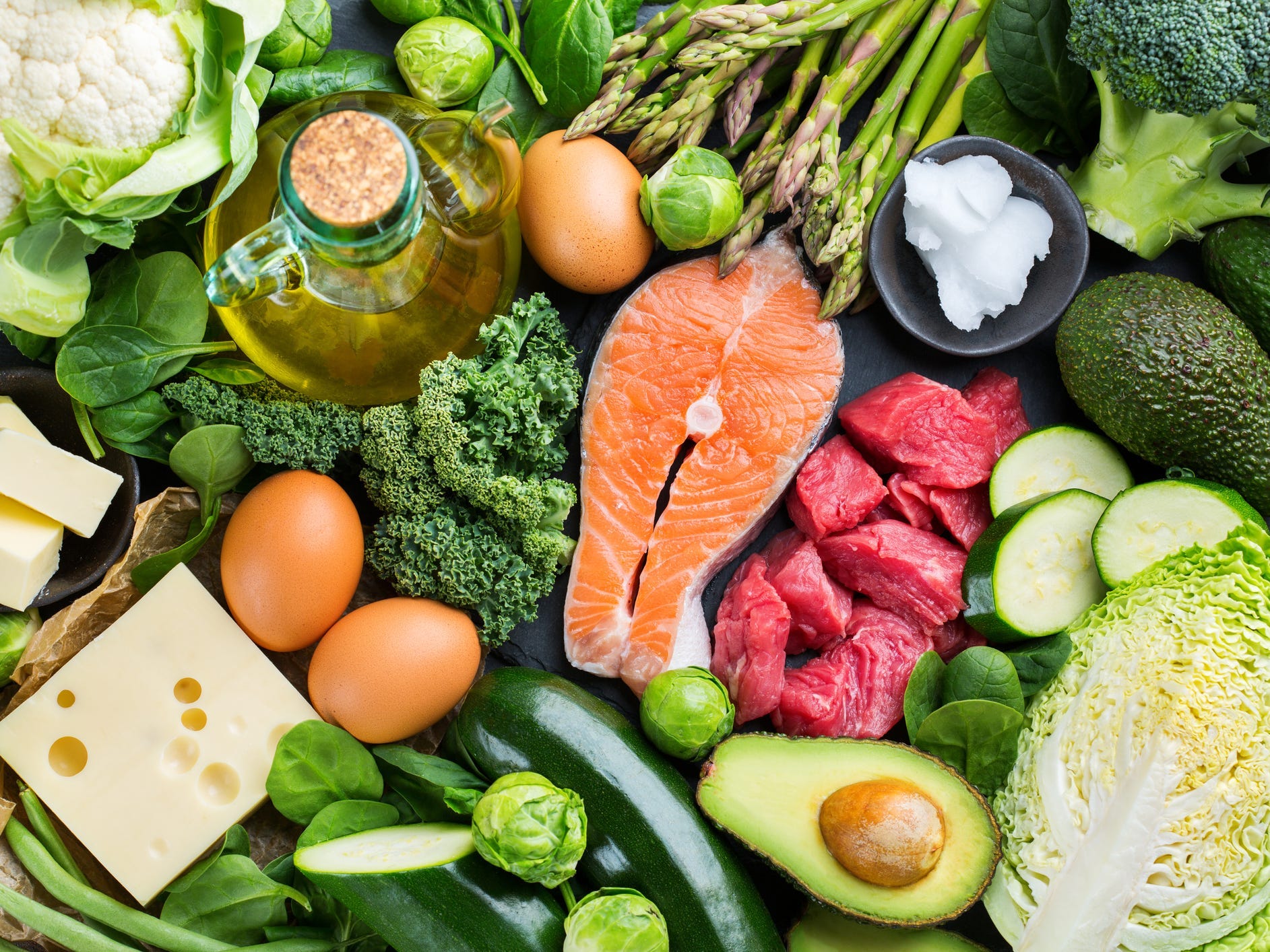 an arrangement of keto diet low carb food, including salmon, oil, beef, eggs, cheese, butter, and green vegetables