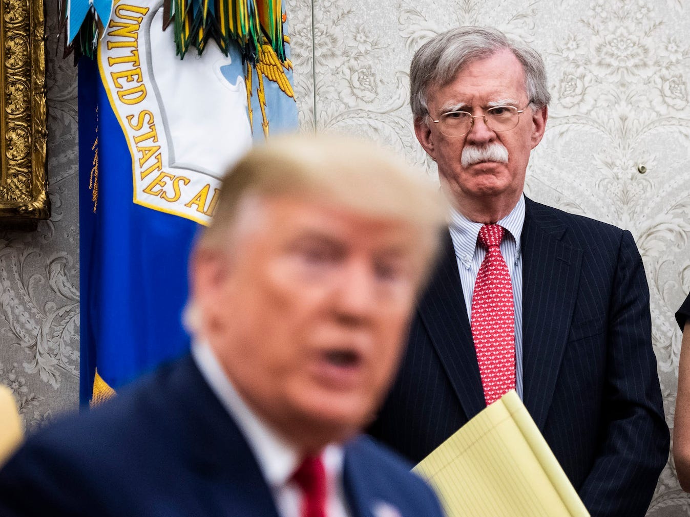 Stephanie Grisham and John Bolton looking at Donald Trump.