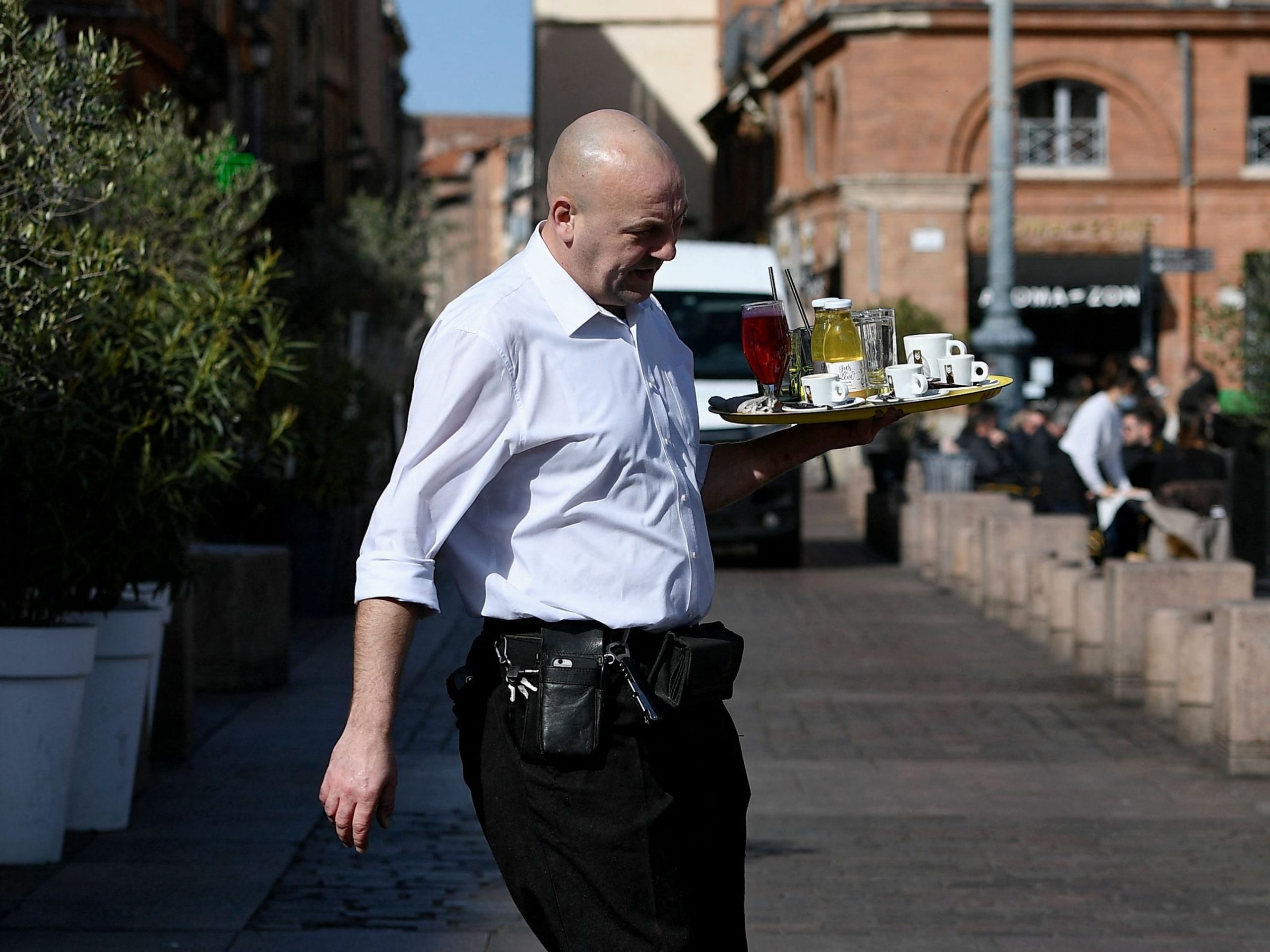 A waiter crosses the road to serve his customers on the terraces set up on the place du Capitole, in Toulouse, southern France, on February 25, 2022.