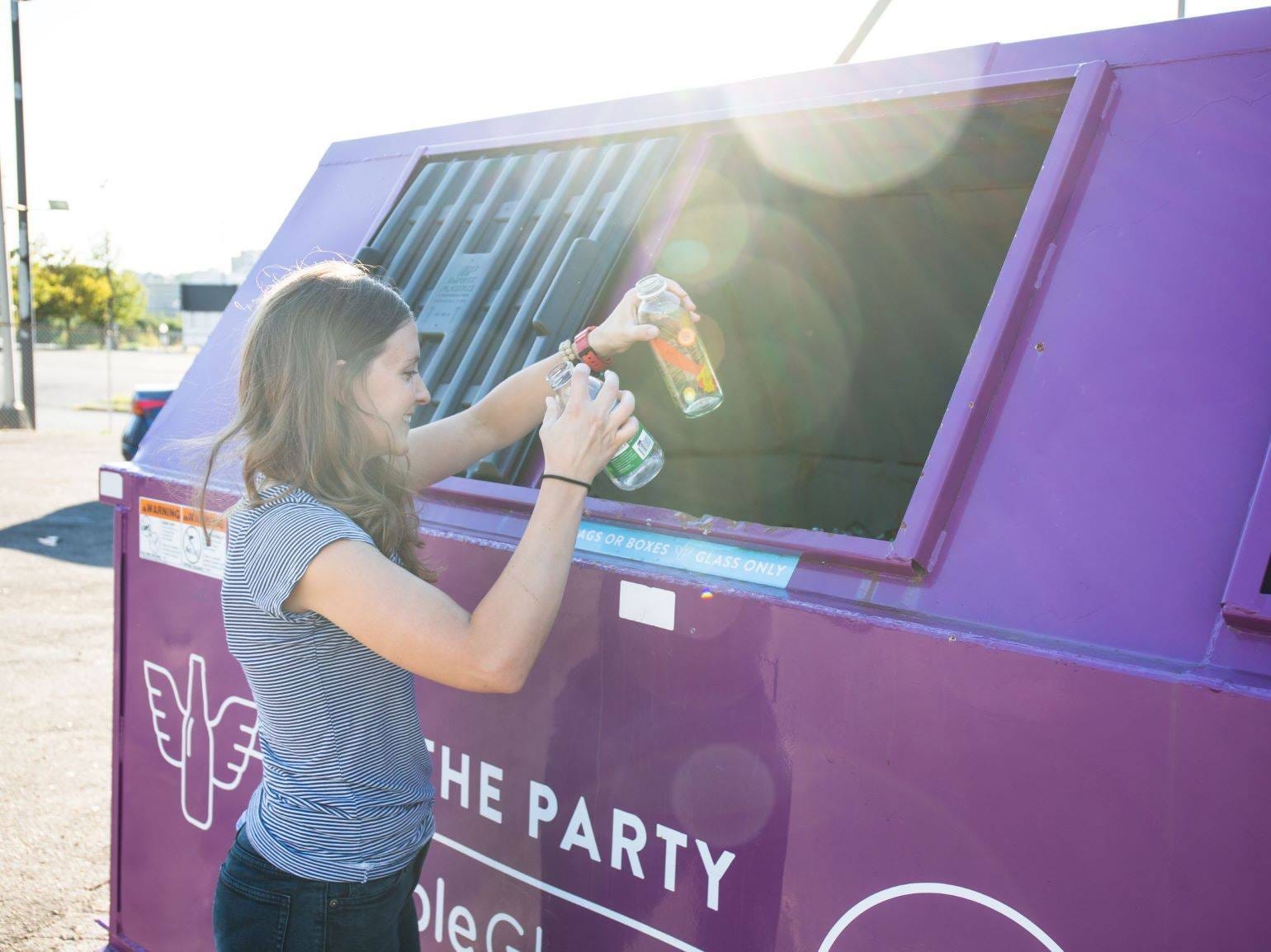 woman tossing glass bottles into recycling bin