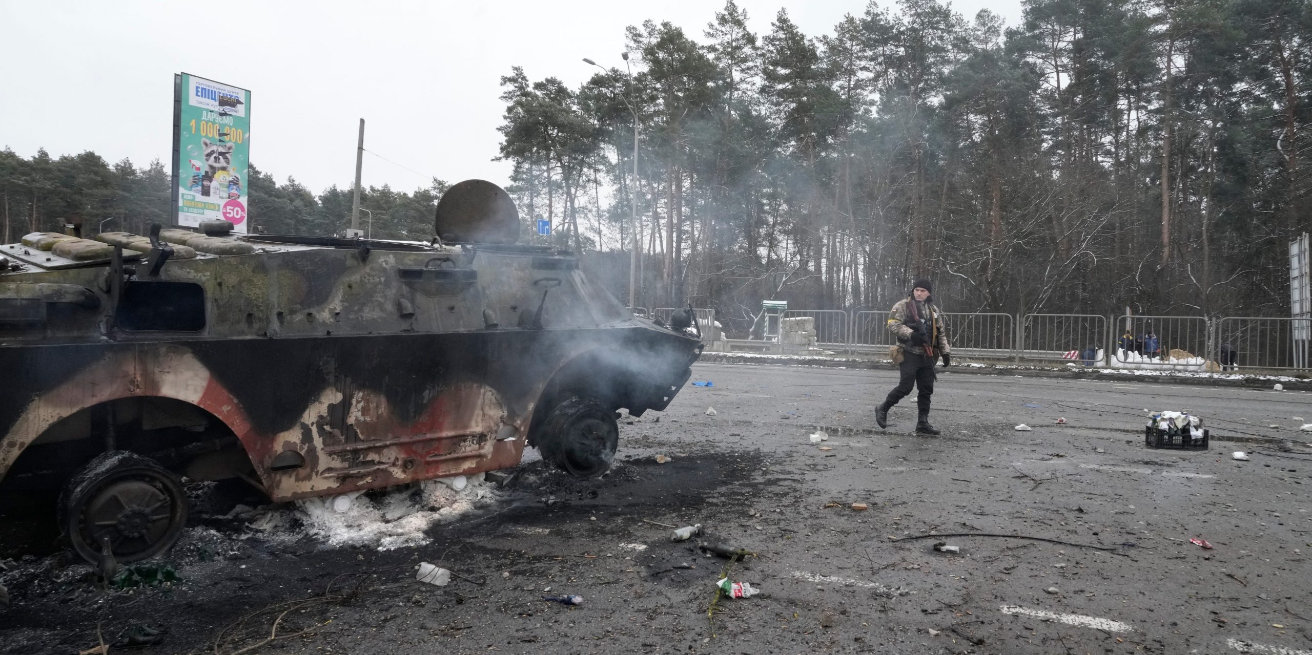 A volunteer of Ukraine's Territorial Defense Forces walks by a damaged armored vehicle at a checkpoint in Brovary, outside Kyiv, Ukraine, Tuesday, March 1, 2022