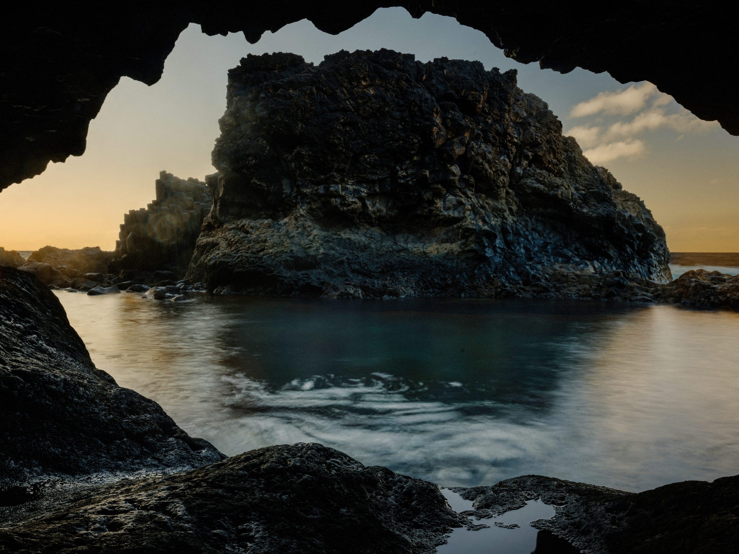 A large rock formation in the ocean at sunset.