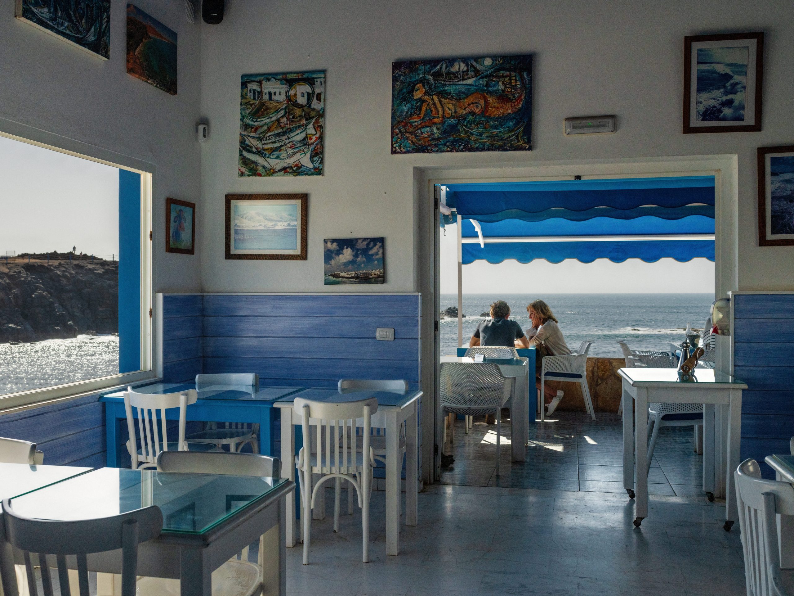 The view of a man and woman sitting at an outdoor terrace of a restaurant from inside.