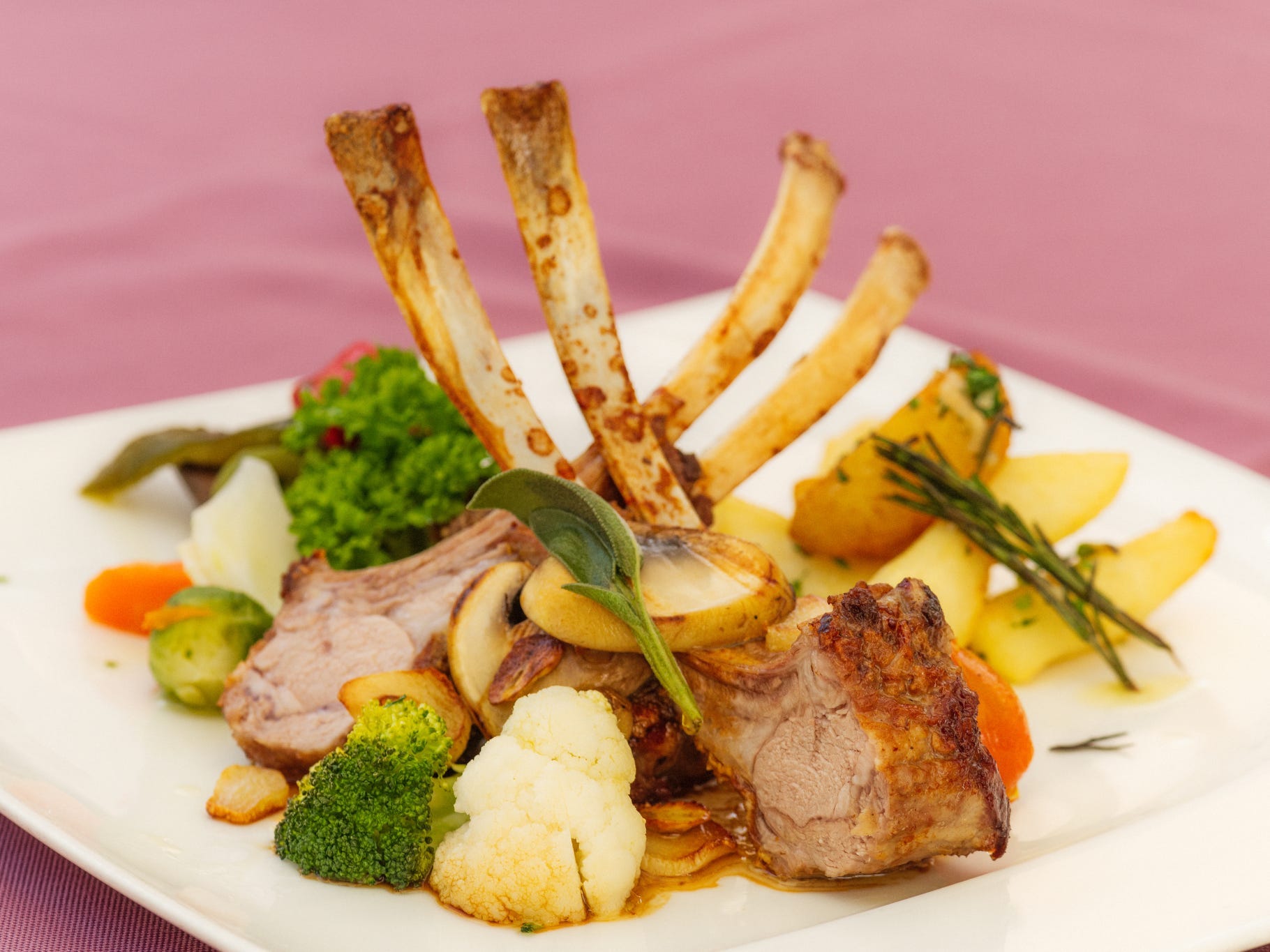 A meal of cooked rib chops on top of vegetables in a small white plate.