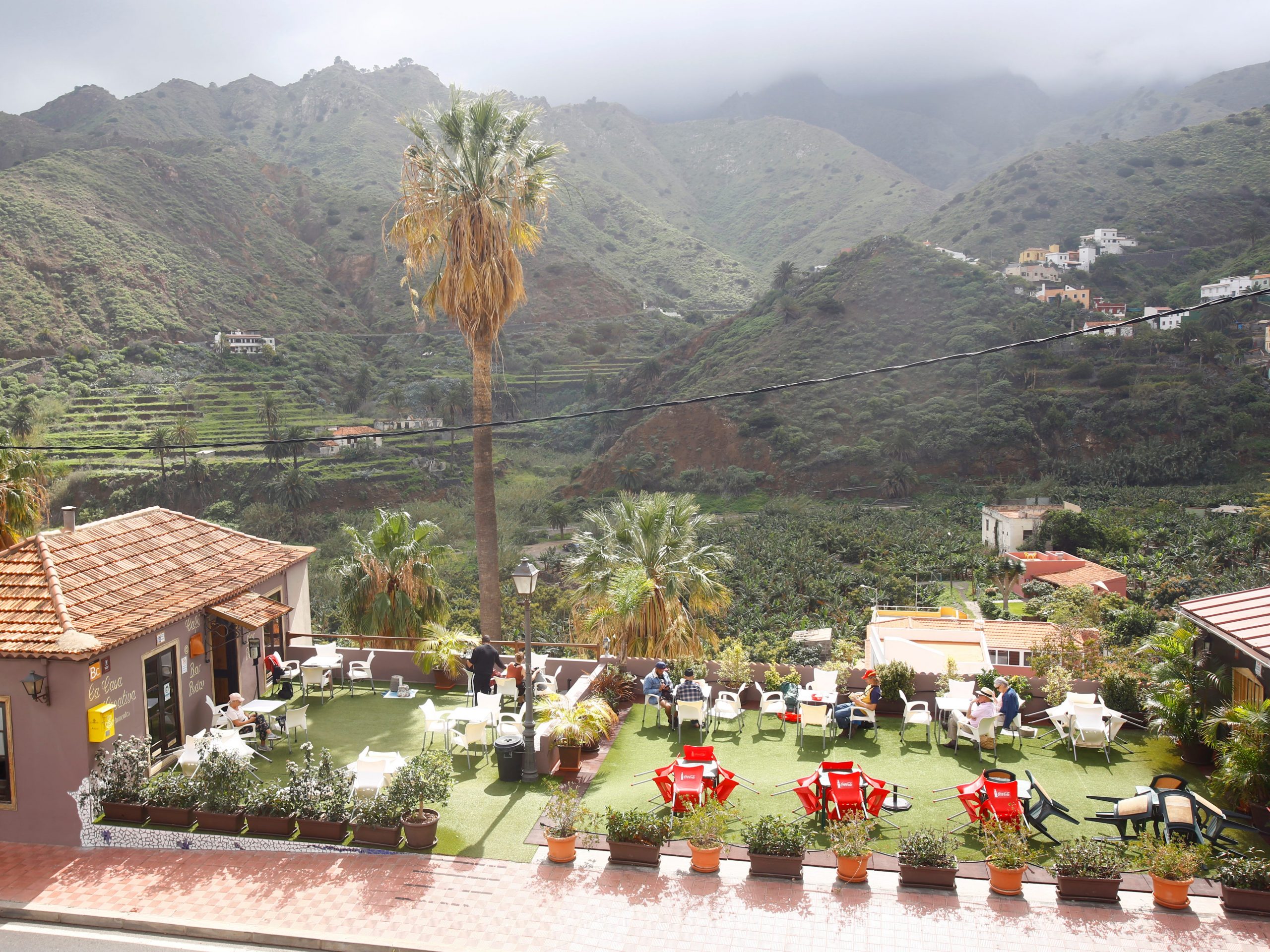 A small restaurant with red tables and chairs behind it in front of a grassy mountain range.