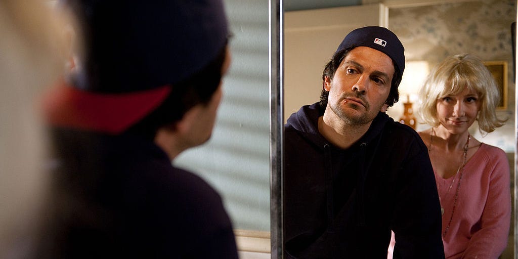 Michael Landes as Tom Harper in the show SAVE ME looks in the mirror at a cold sore on his lip.