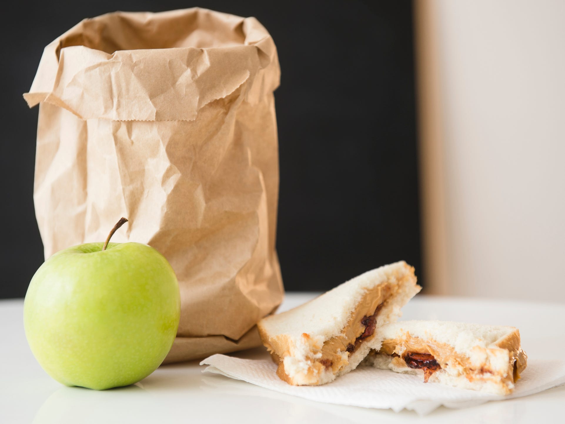 brown paper bag on a table with an apple and a pb&j