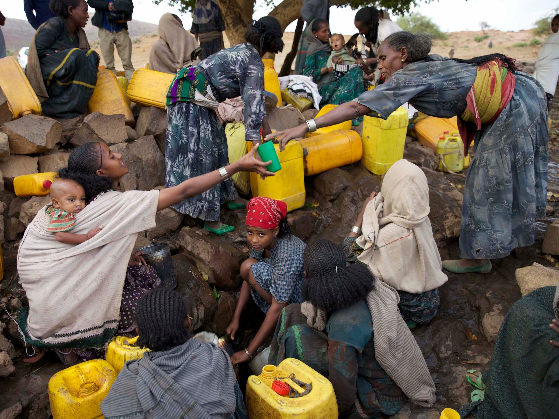 women surrounded by large yellow jugs collect water from a muddy stream some carrying babies