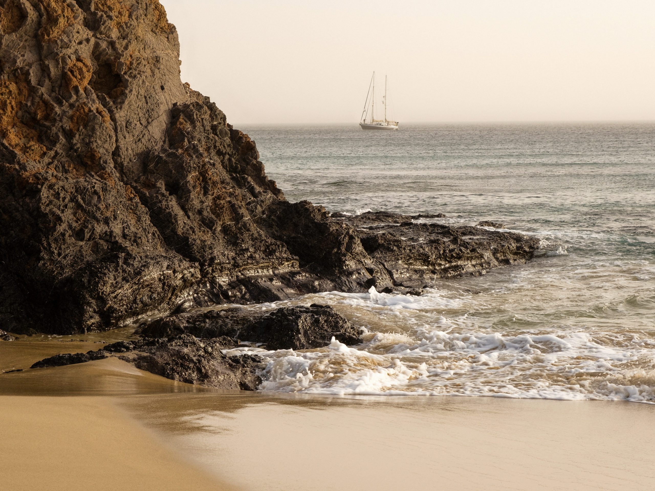 A large rock face on a beach bordering the ocean.