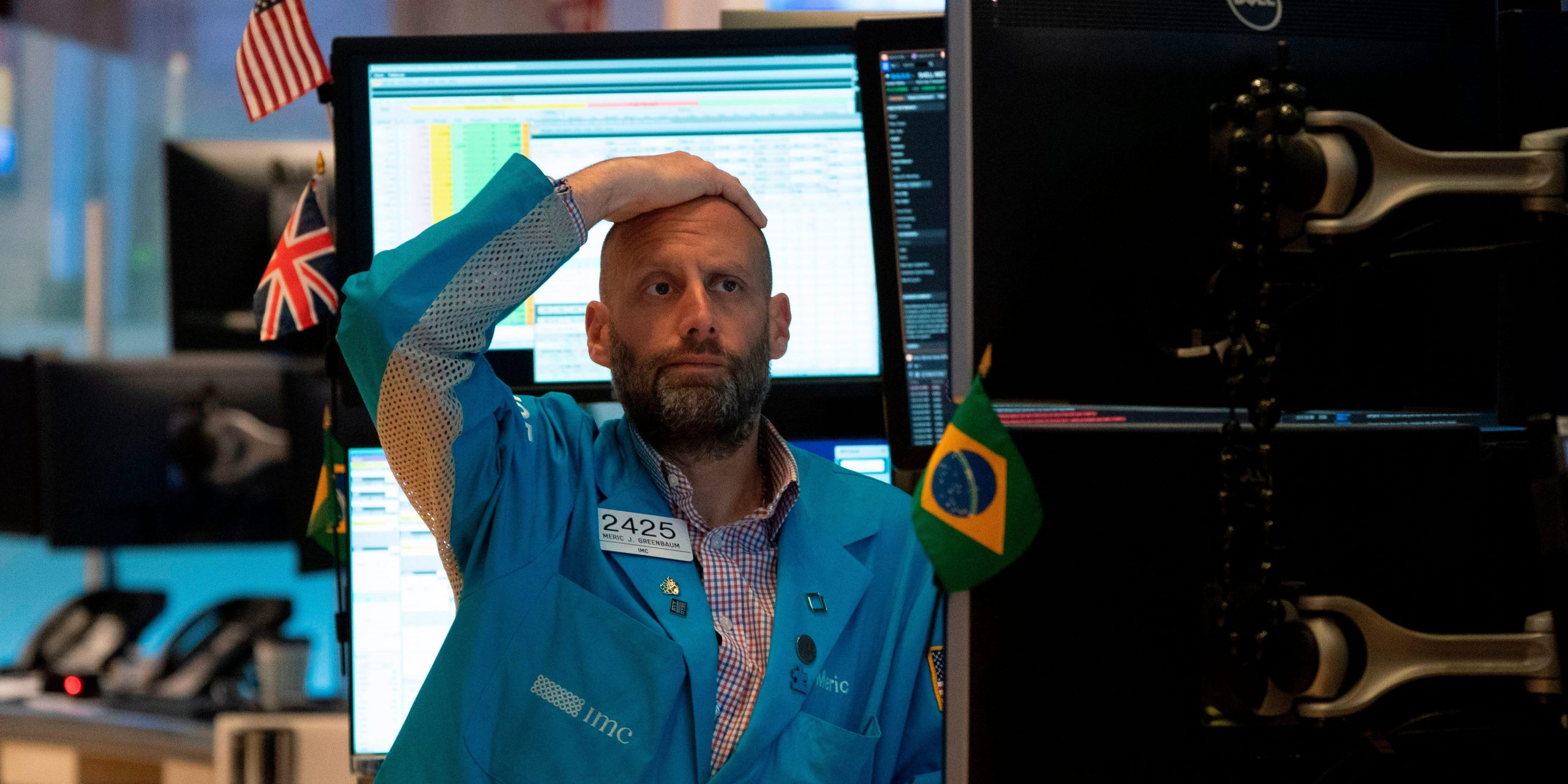 A trader looks distressed while staring at a computer screen, with his hand on his head.