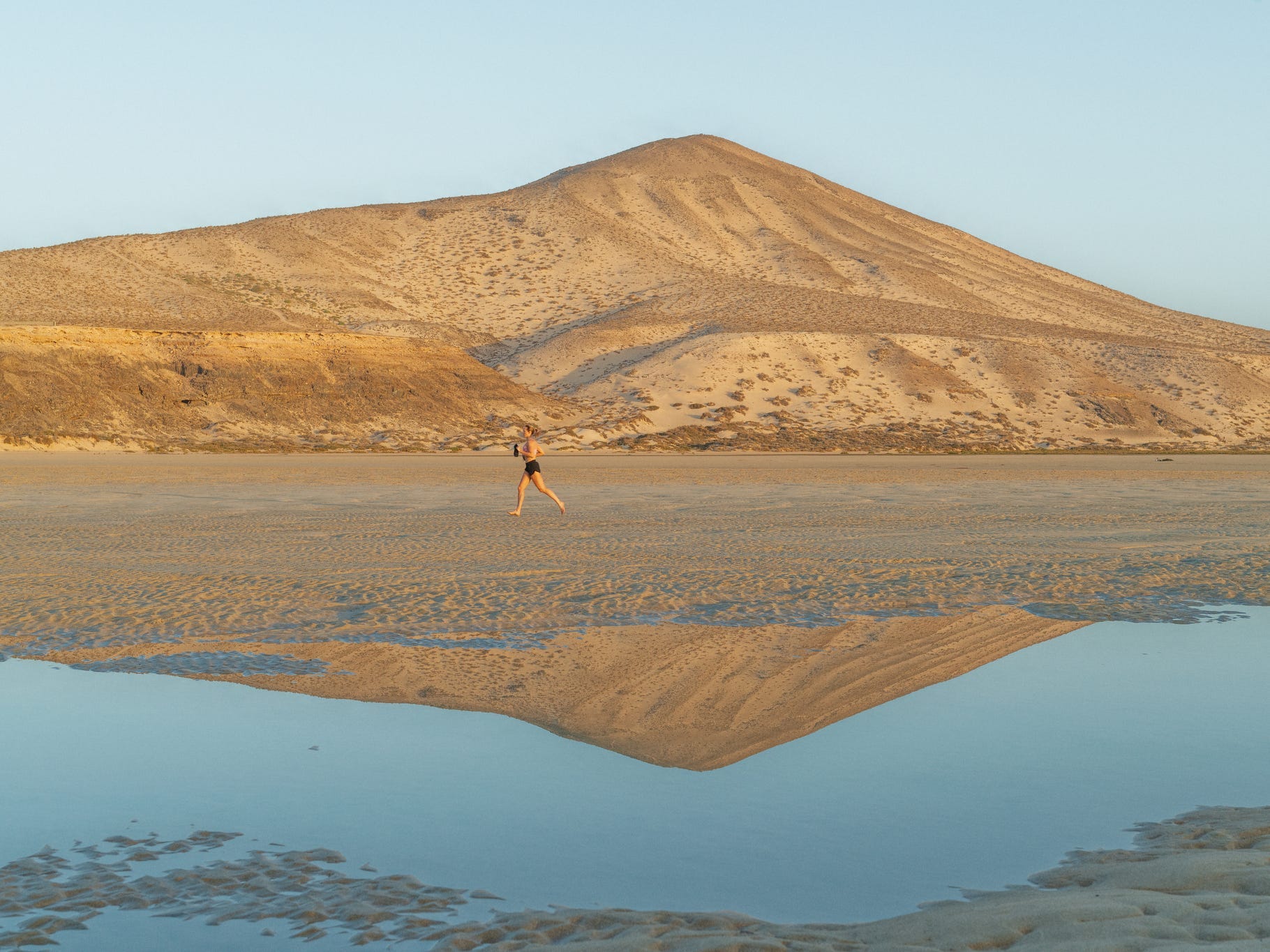 A woman running on the beach in front of a large sandy hill.