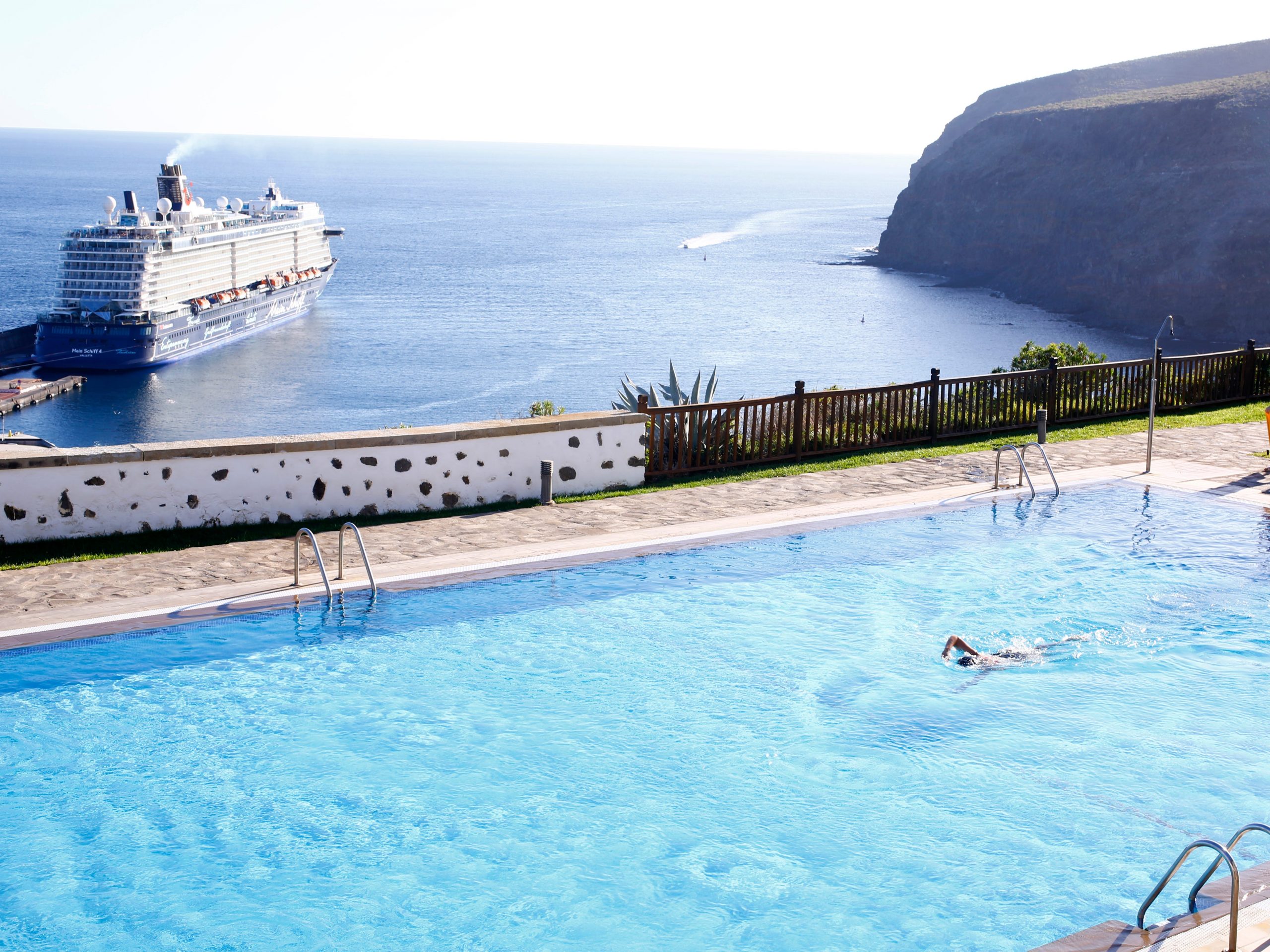 Someone swimming in a pool overlooking the sea with a cruise ship in the distance in the Canary Islands