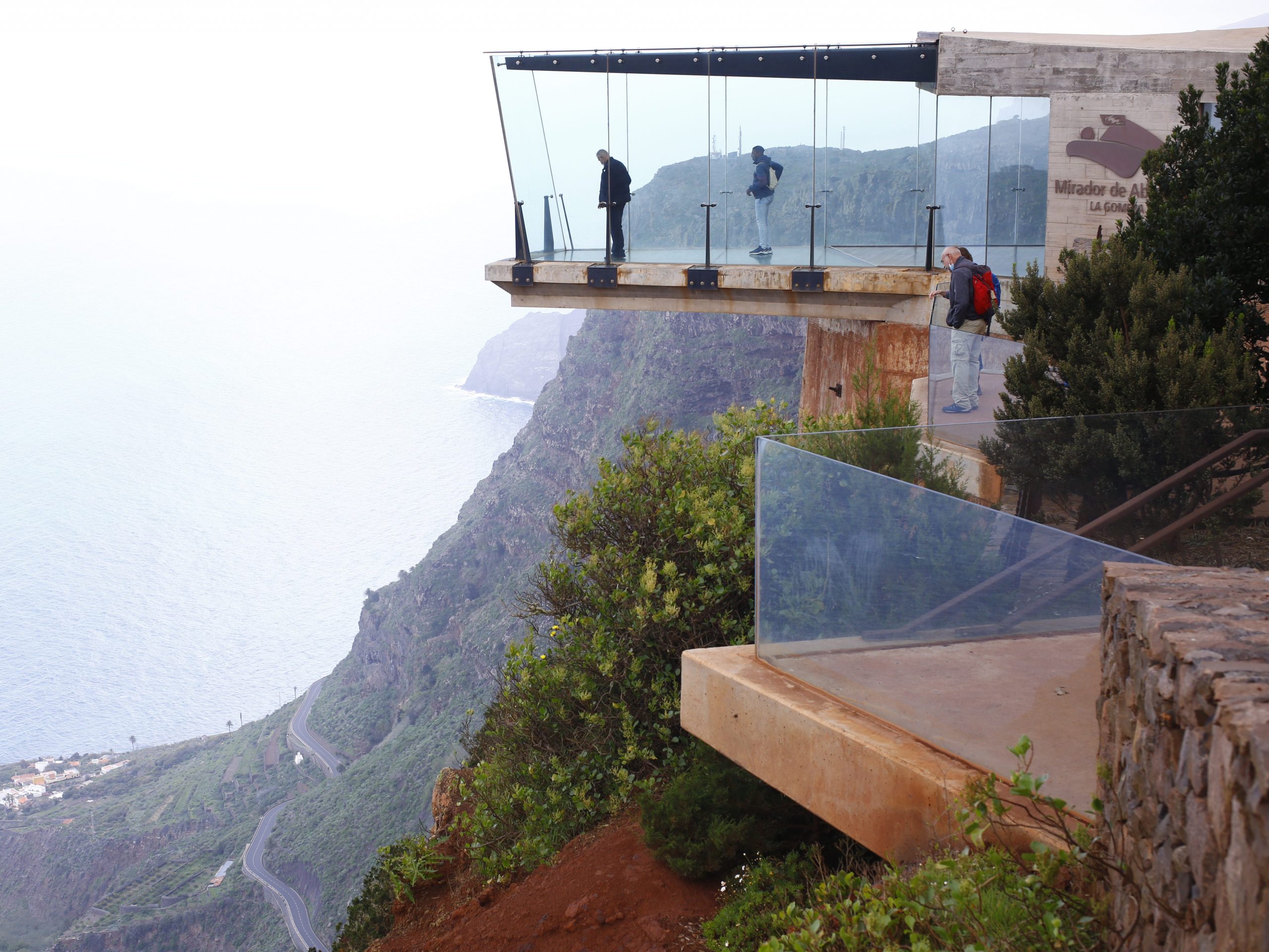 People standing in a glass overhang overlooking a mountain vista.