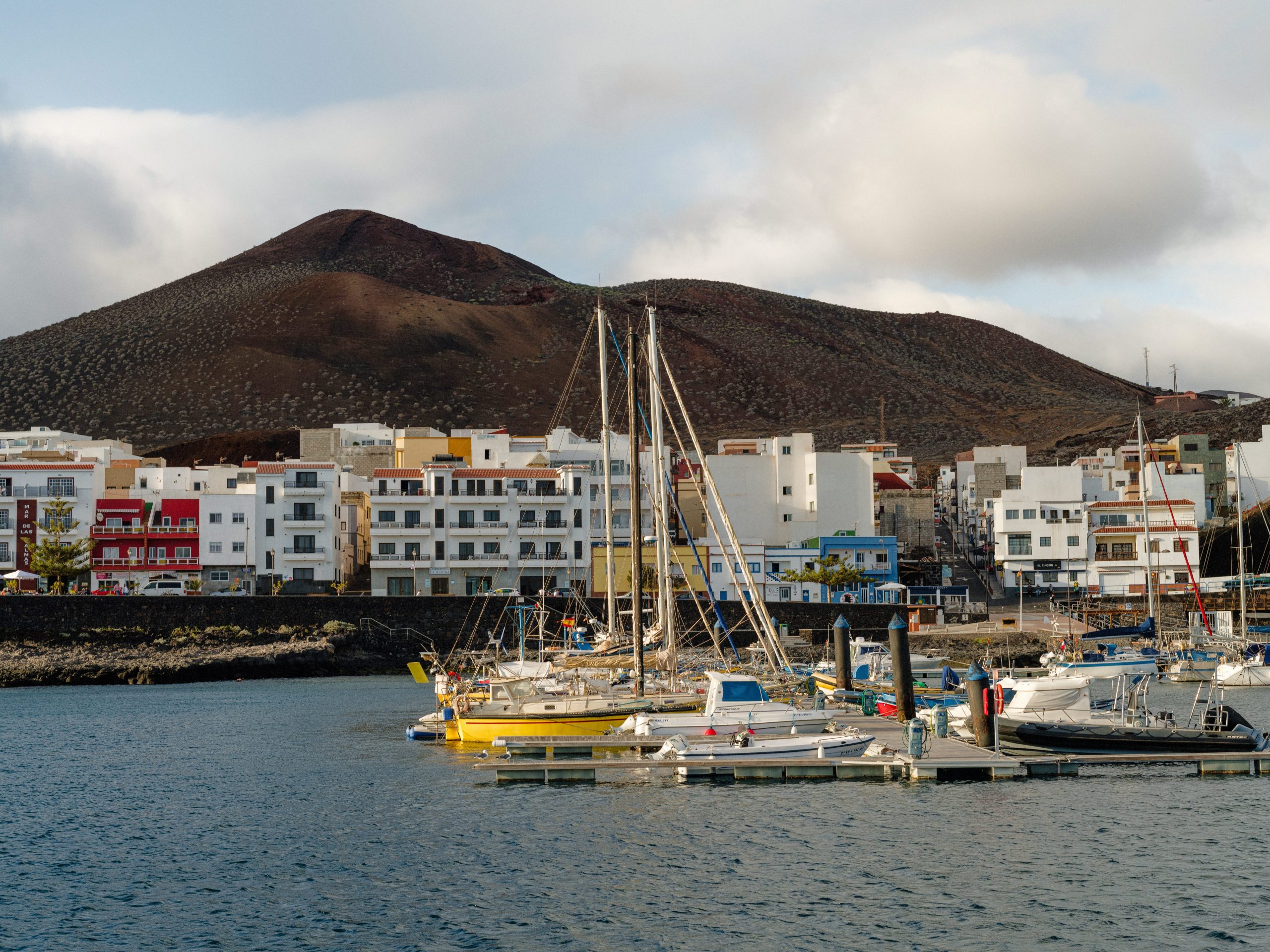 Several boats docked in the water in front of the tall white buildings of a town.