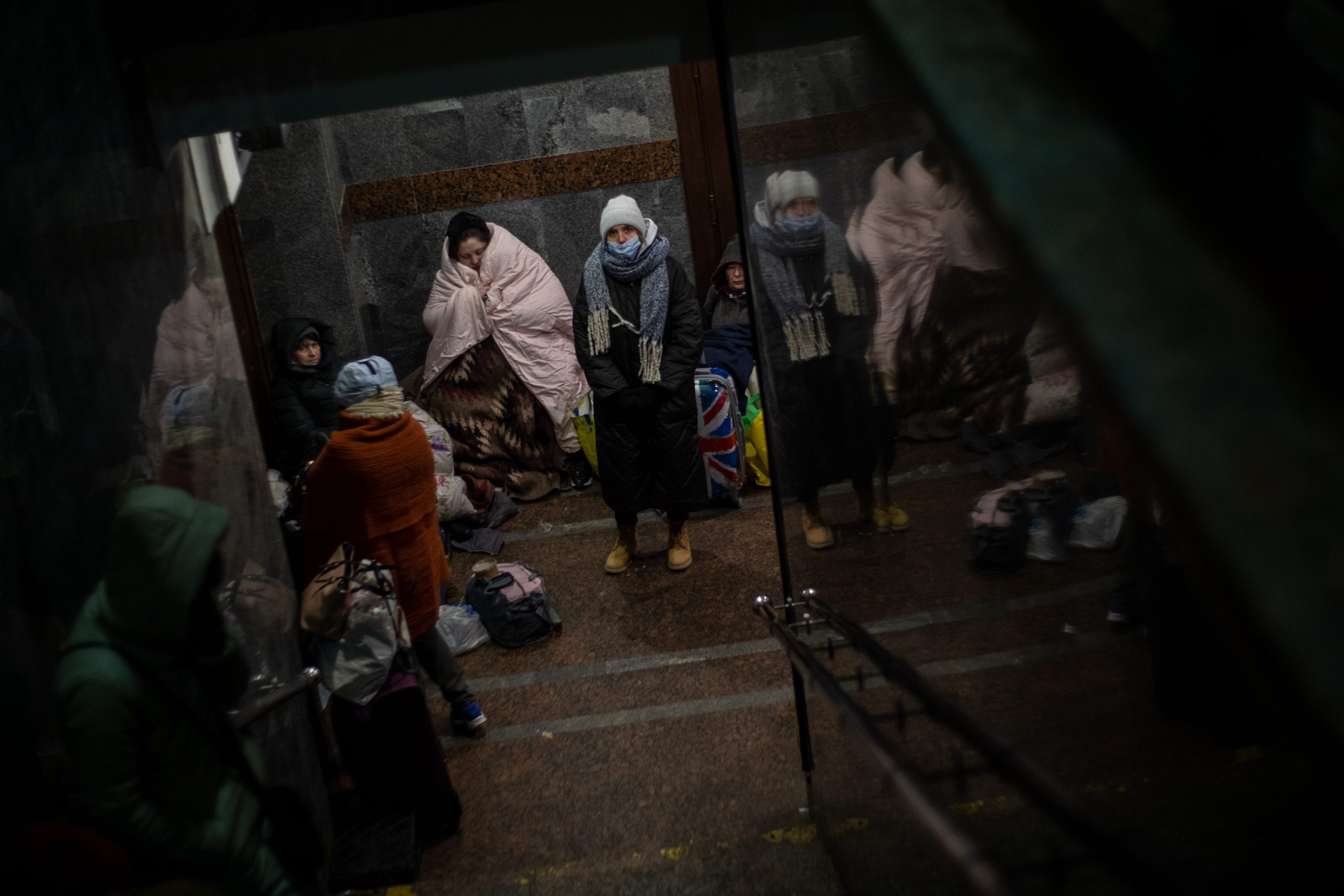 People are seen huddled for warmth at the bottom of a staircase at a train station.