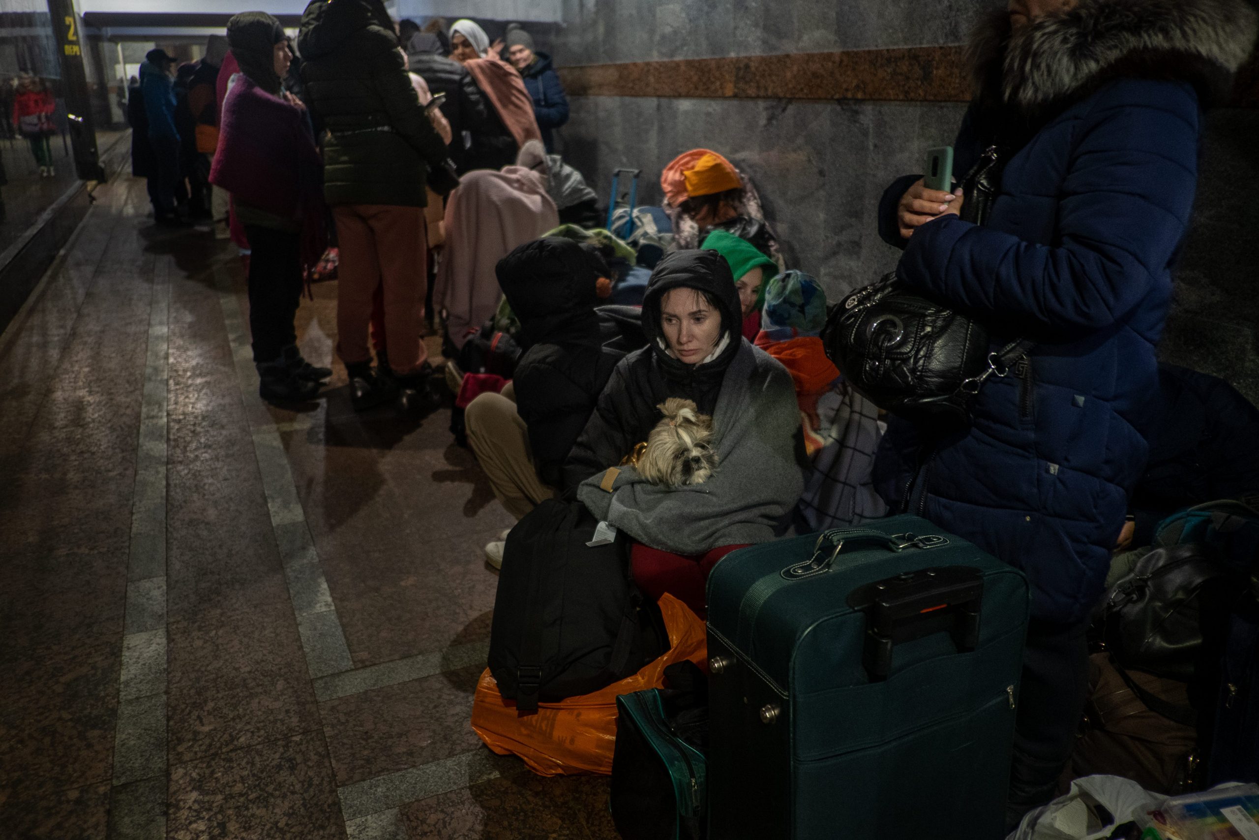 People are seen crammed together on a darkened train platform.