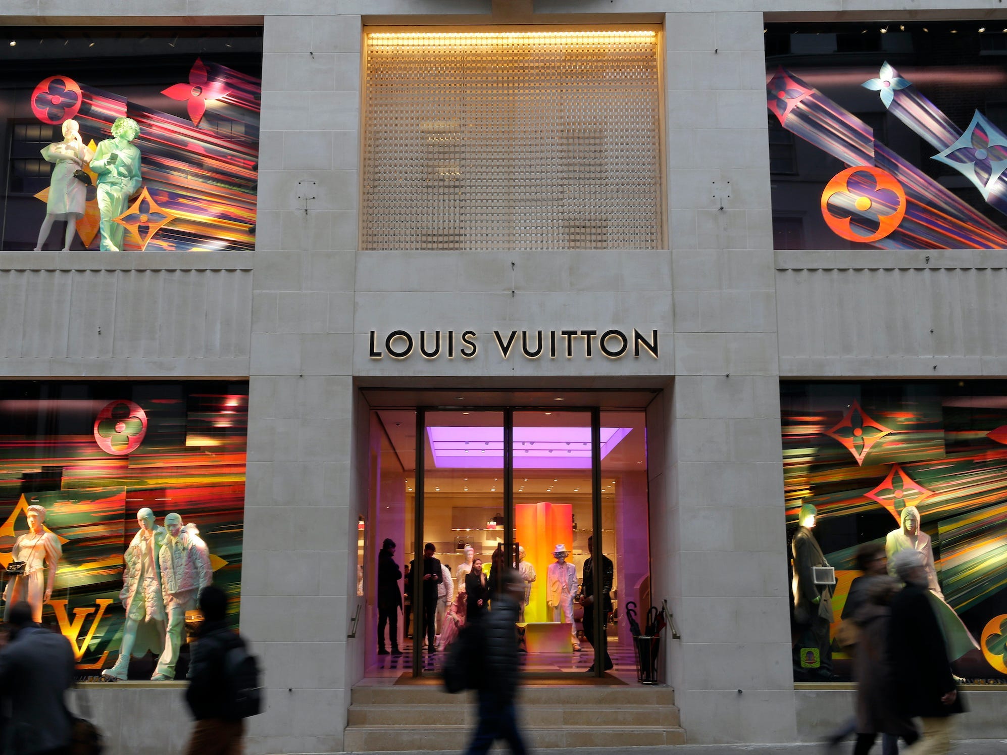 Shoppers walk by Louis Vuitton store in London with colorful window displays