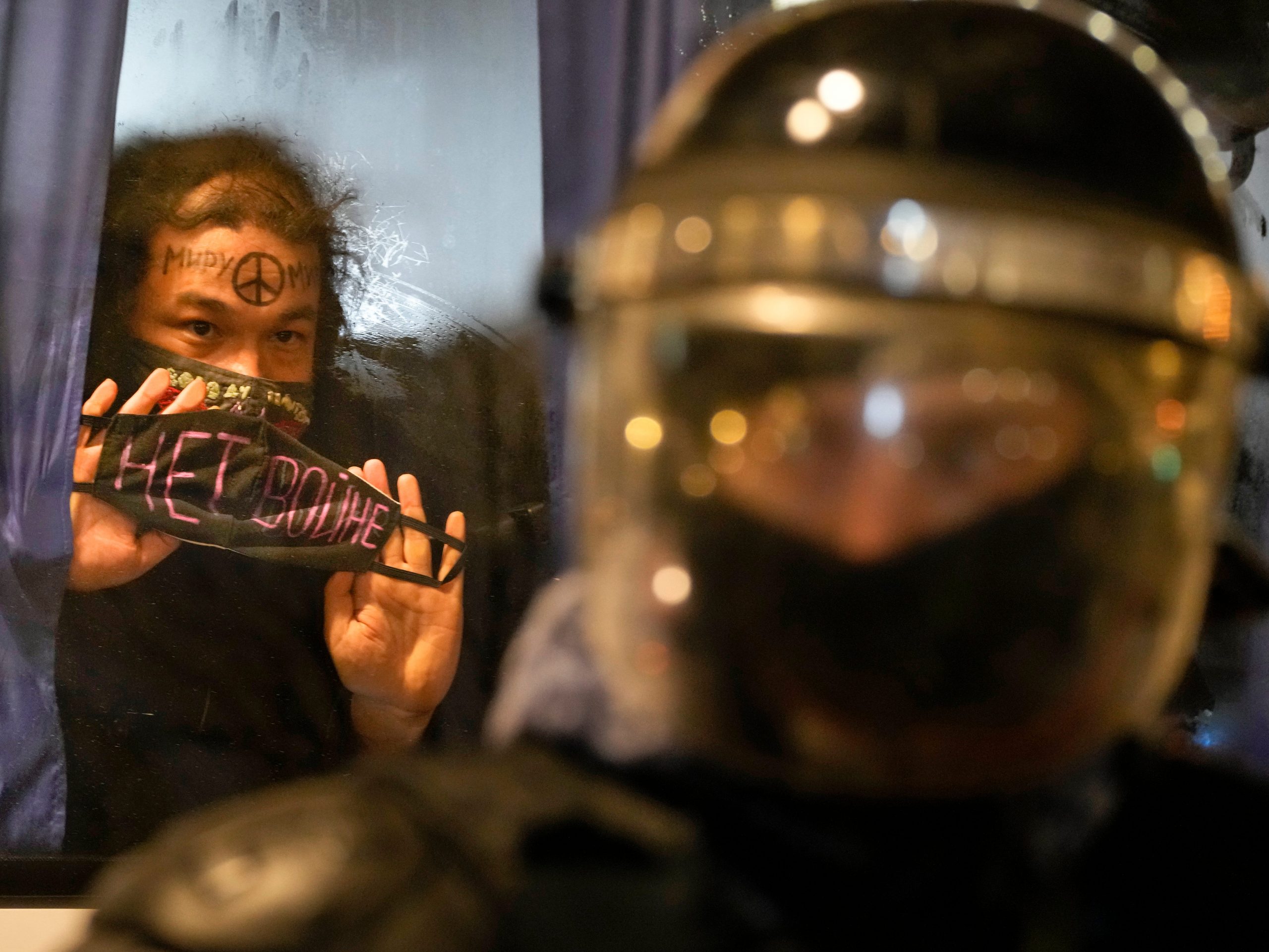 A detained demonstrator shows a sign 'No War!' from a police bus in St. Petersburg, Russia.