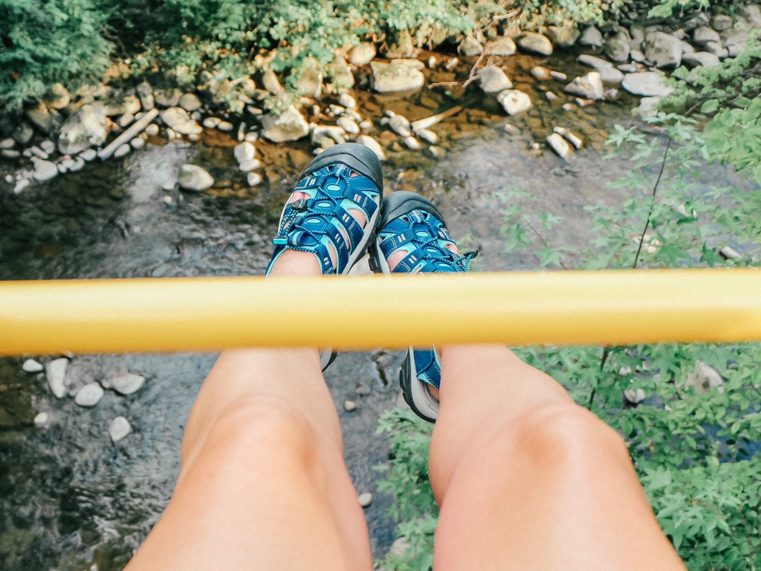 A photo of legs dangling over a bridge with blue comfy shoes