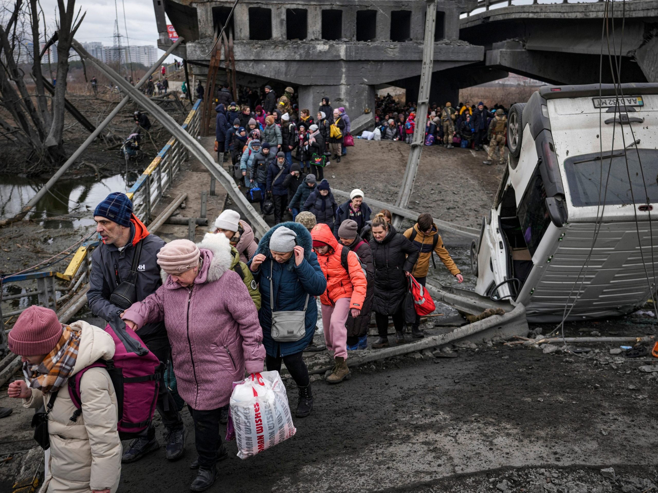 People cross on an improvised path under a bridge that was destroyed by a Russian airstrike, while fleeing the town of Irpin, Ukraine, Saturday, March 5, 2022.