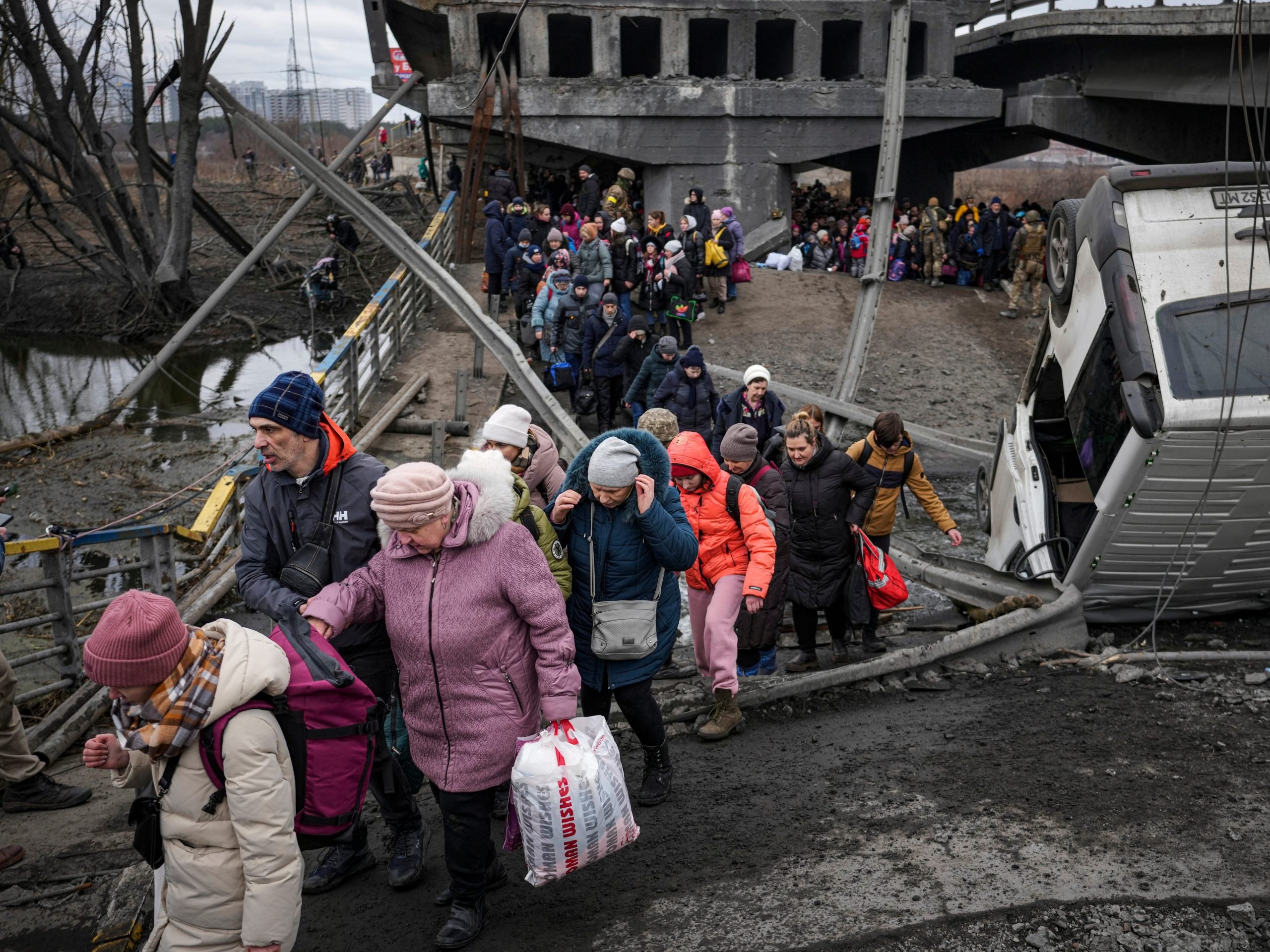 People cross on an improvised path under a bridge that was destroyed by a Russian airstrike, while fleeing the town of Irpin, Ukraine, Saturday, March 5, 2022.