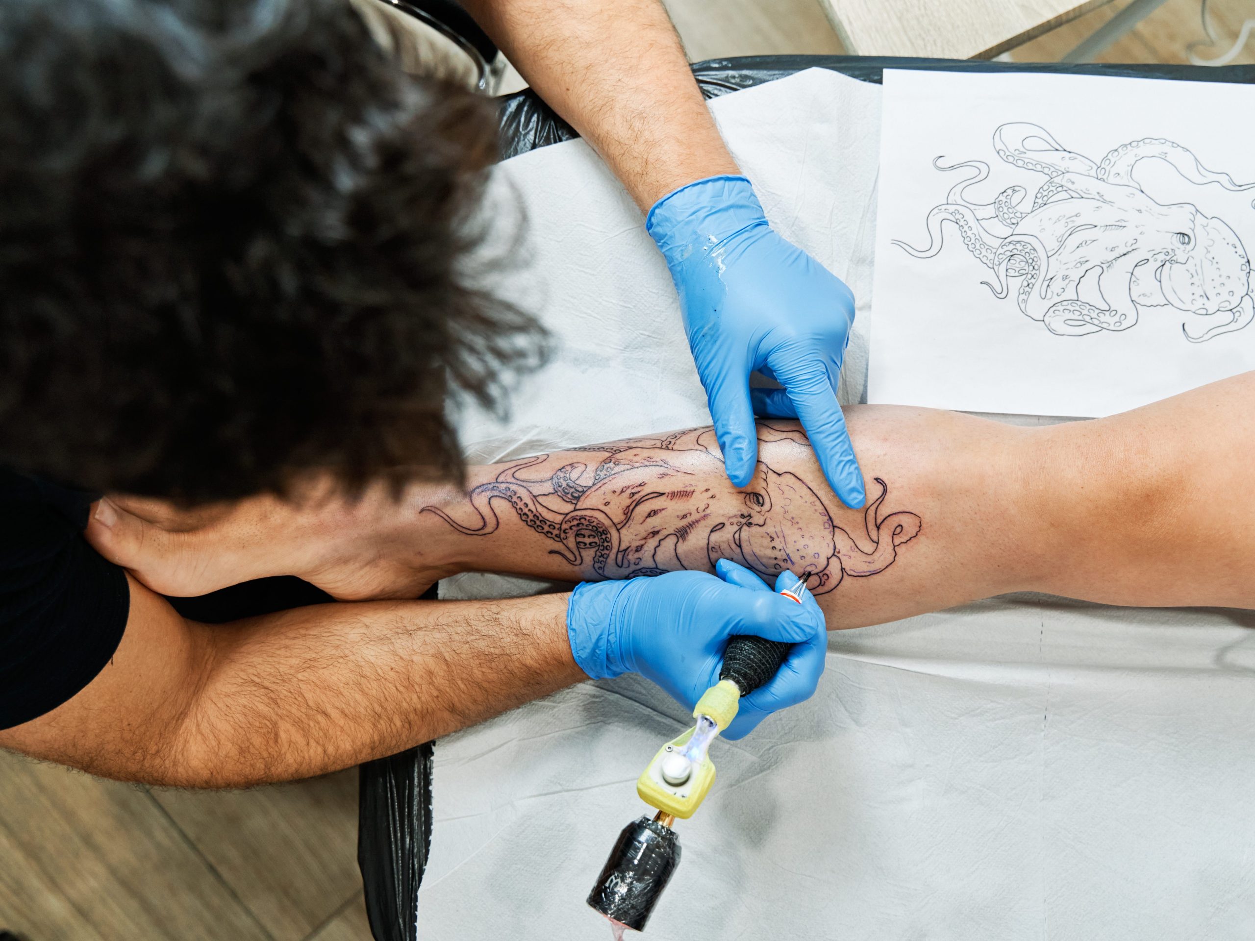 Tattoo artst inking octopus design on client's leg
